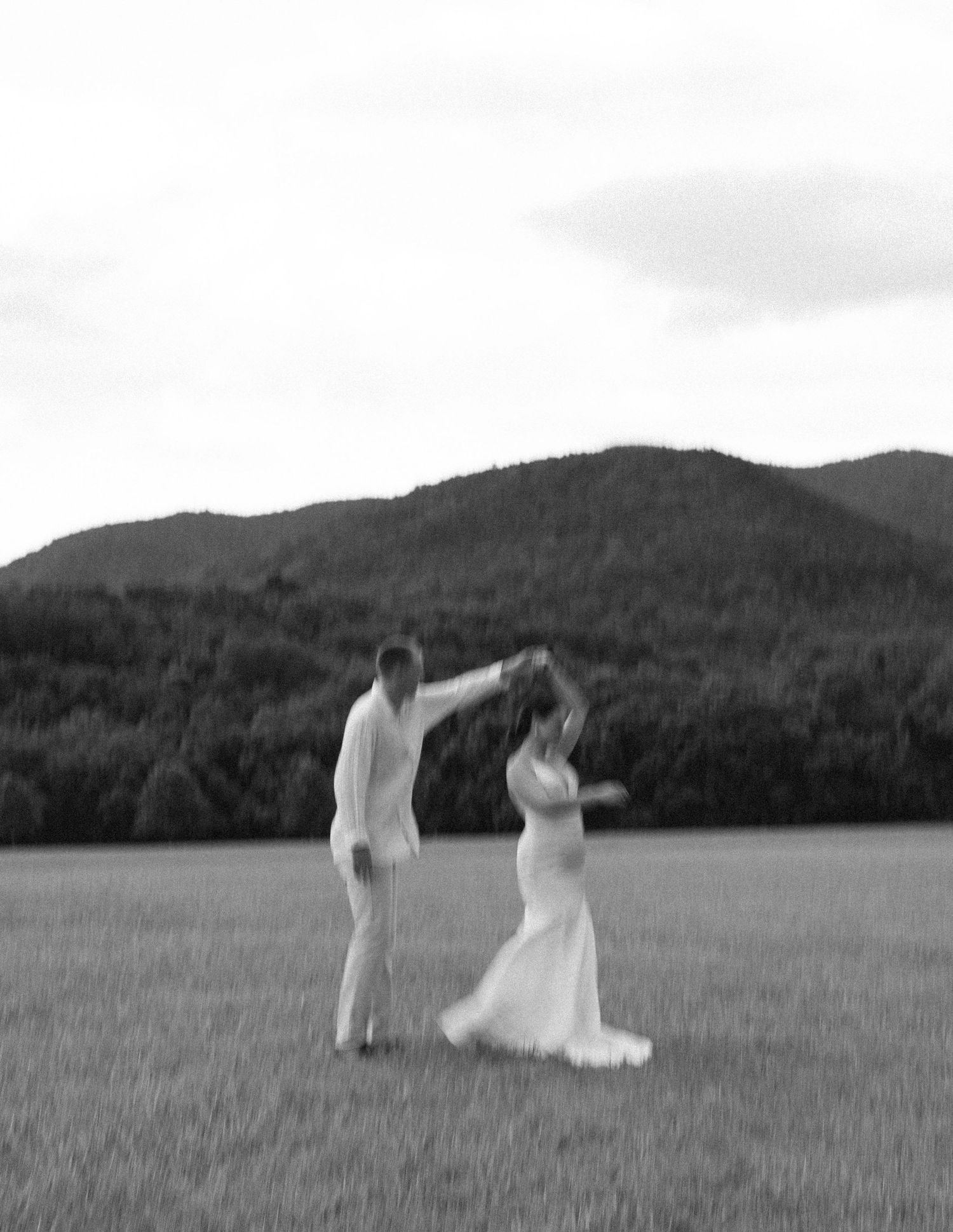 Couple dancing in an open field with mountain landscape behind them.