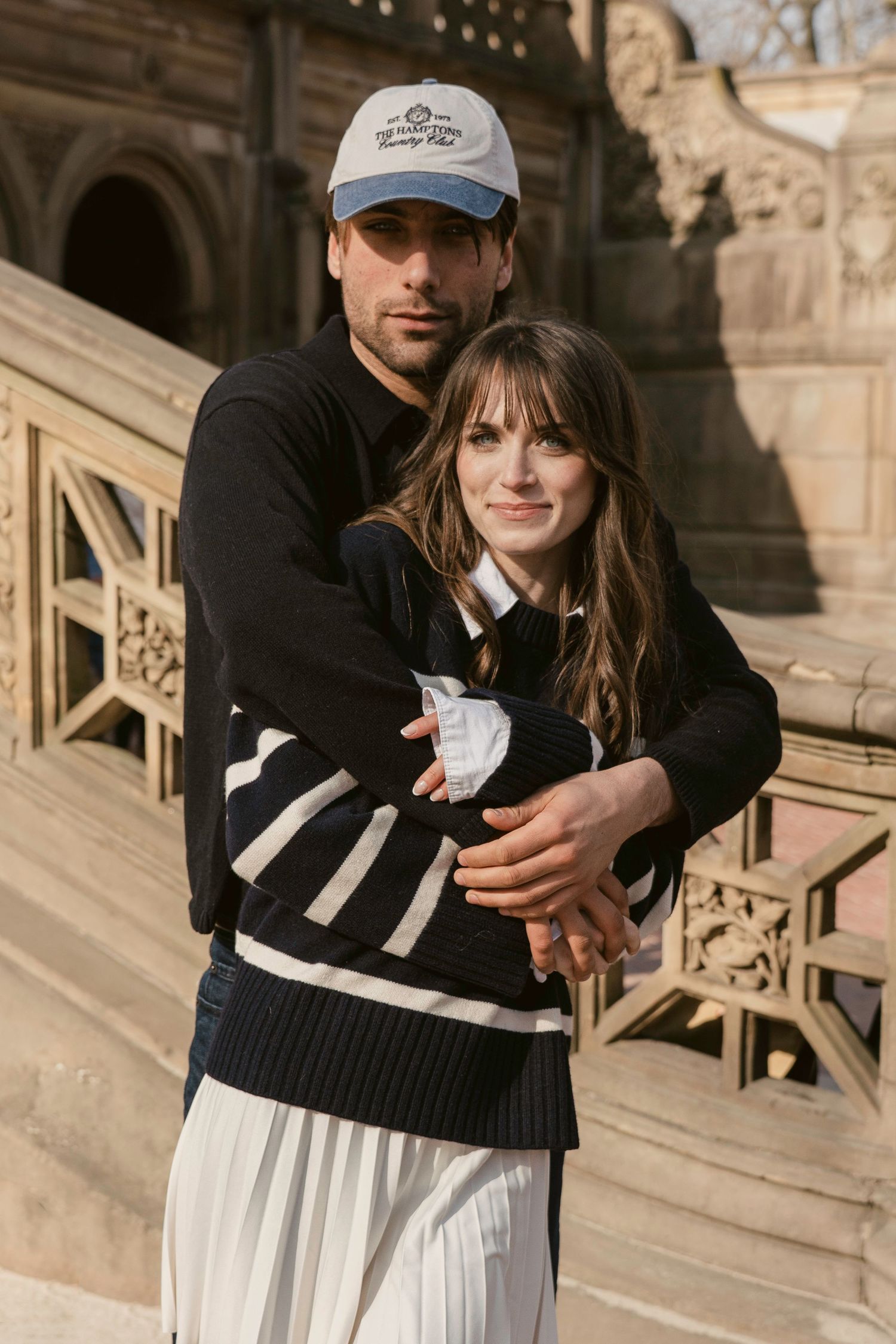 Couple in casual winter outfits embracing on ornate stone steps.