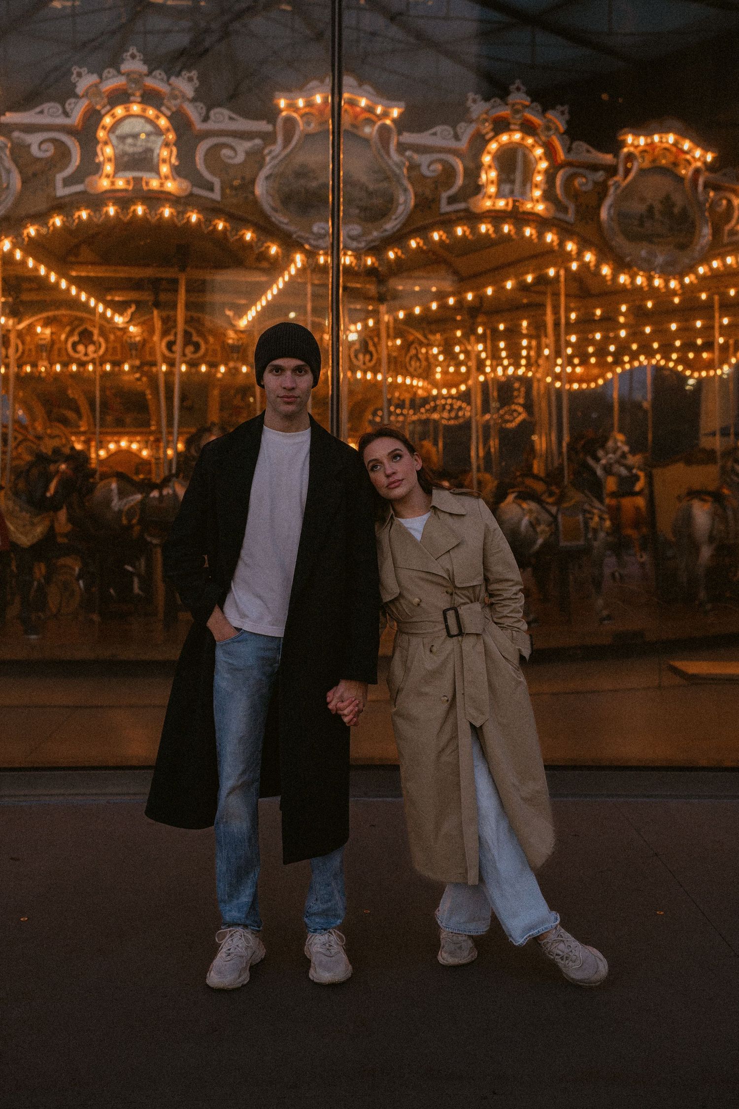 Couple enjoying evening at carnival with illuminated carousel lights in background.