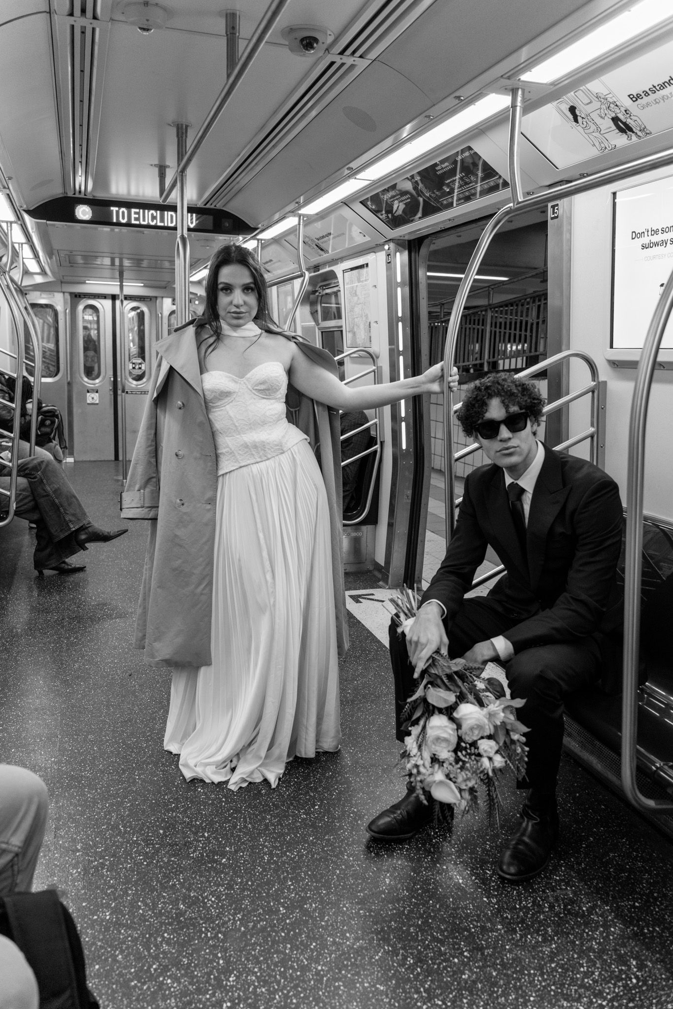 Wedding couple posing in empty subway car with formal attire and bouquet.