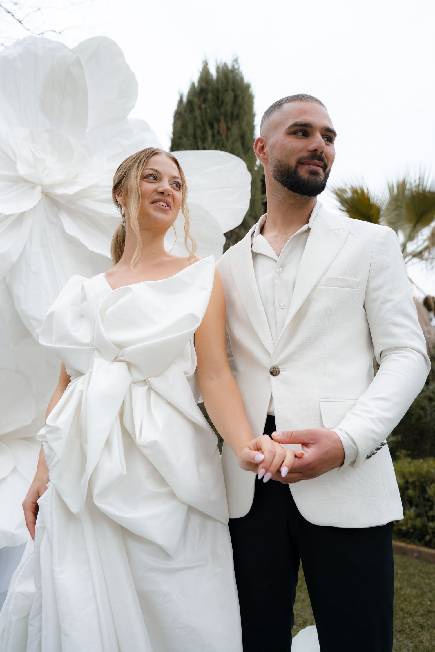 Candid wedding portraits in all-white attire against a garden backdrop.