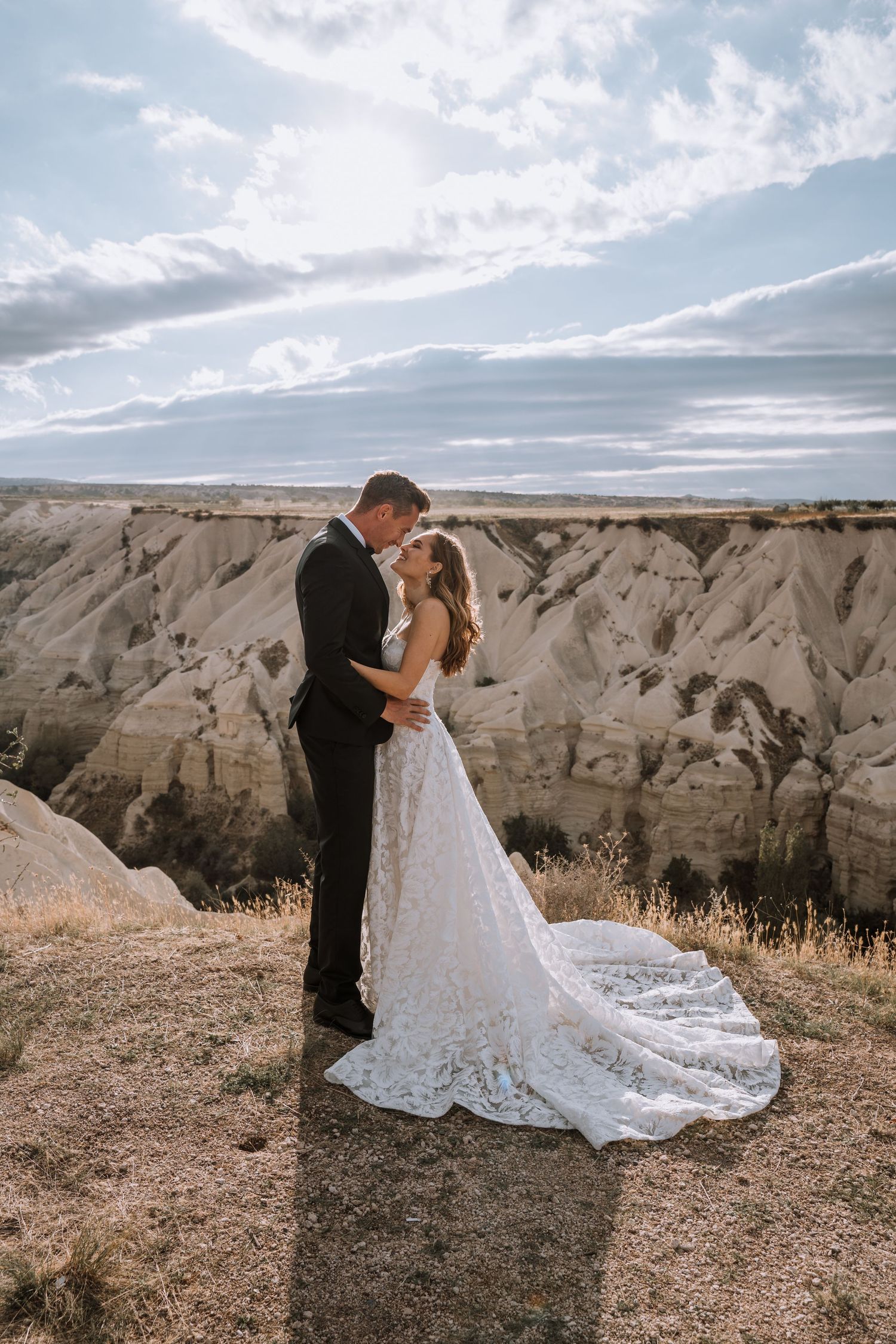 A wedding couple embraces against a dramatic desert cliff backdrop.