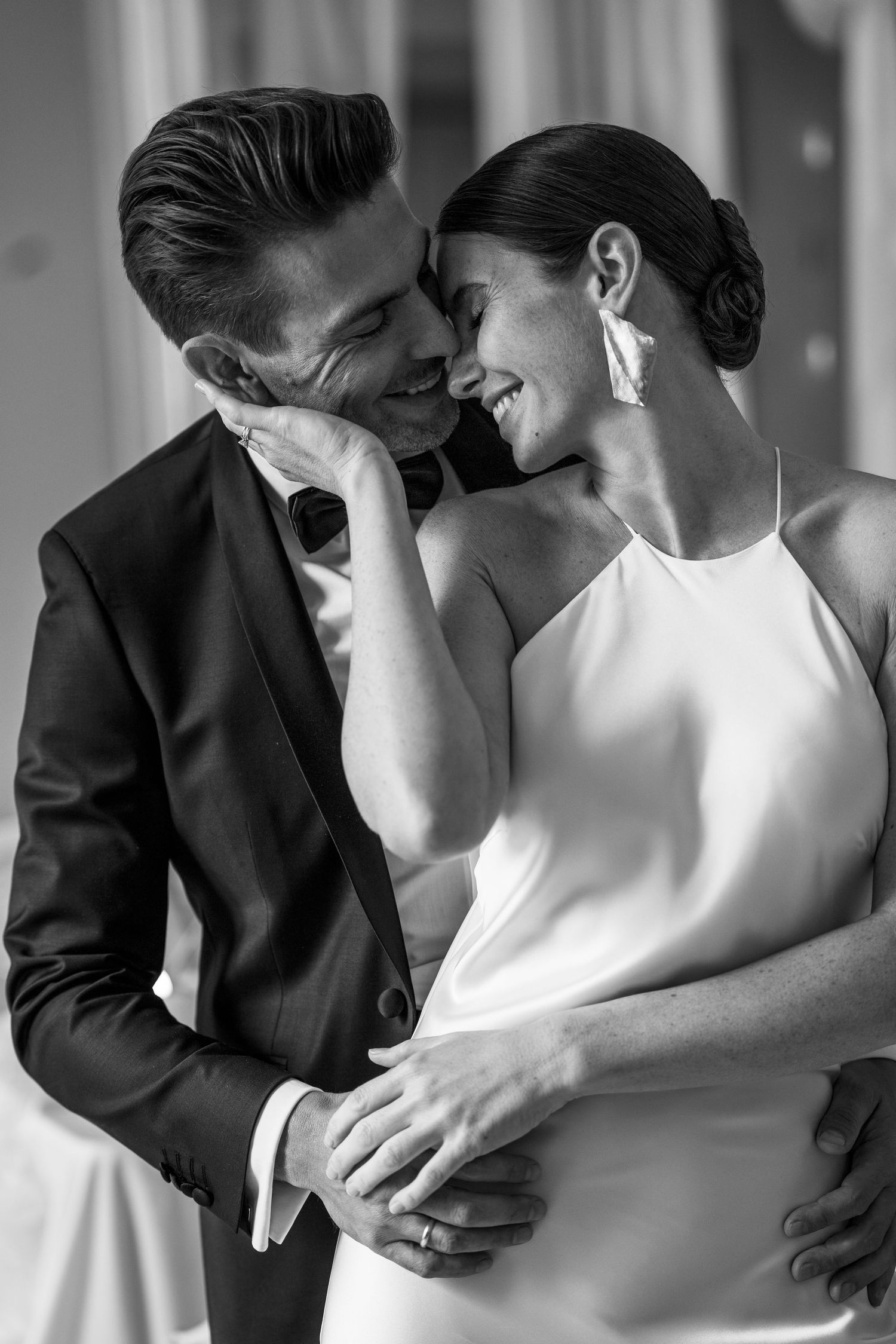 Intimate black and white portrait of newlyweds sharing a tender moment in formal attire.