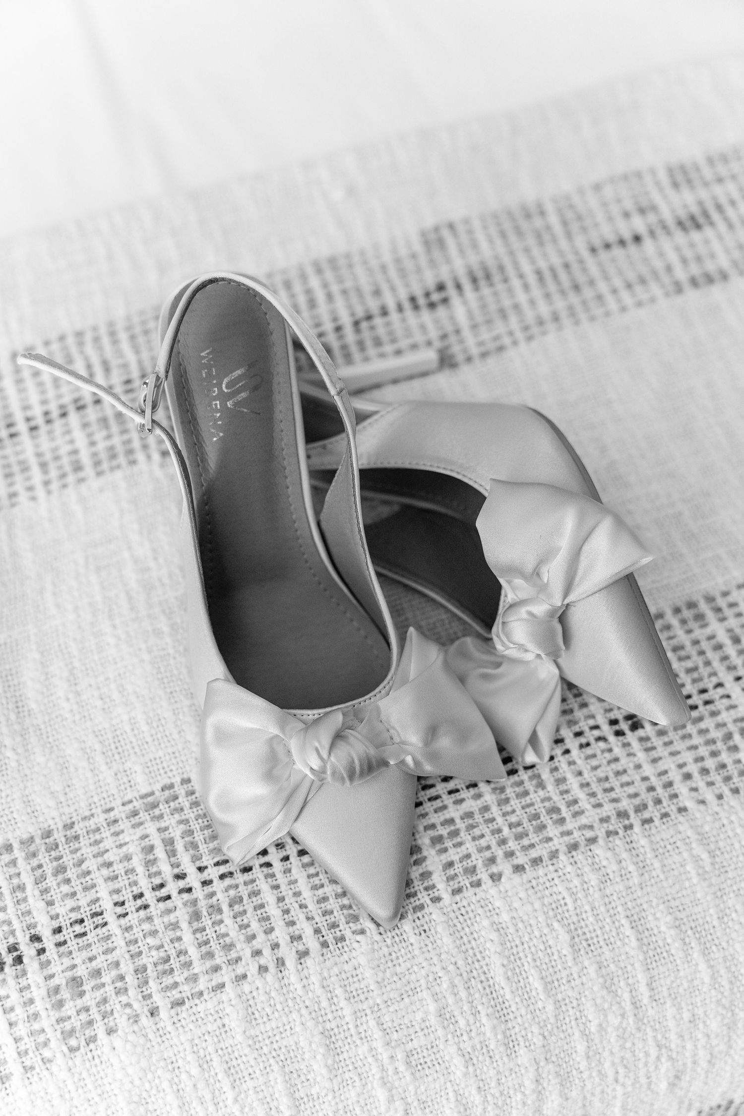 Delicate white ballet shoes with ribbons arranged on textured fabric.