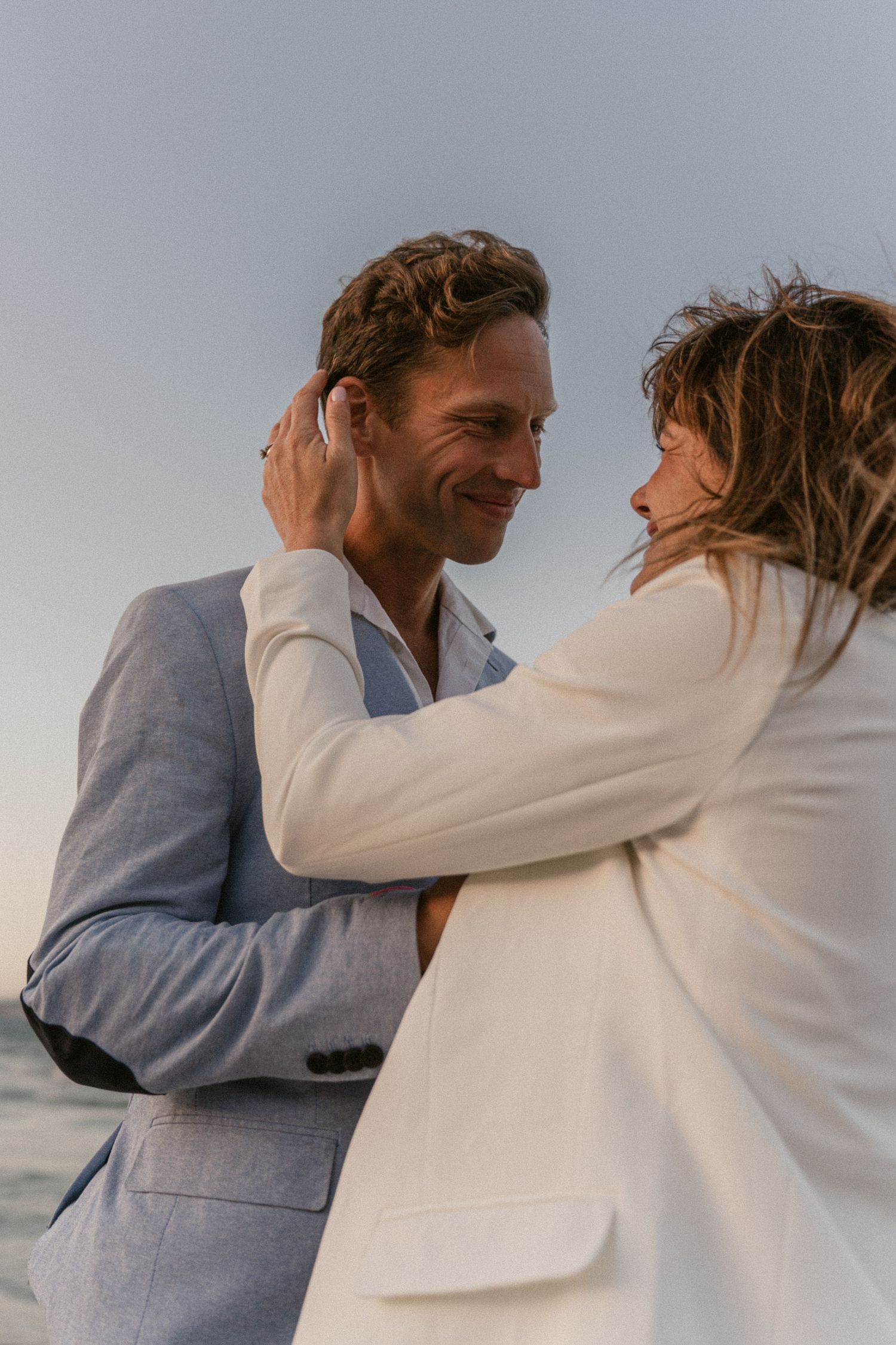 A romantic couple in beige and blue attire embrace in a series of tender moments against a soft sky background.