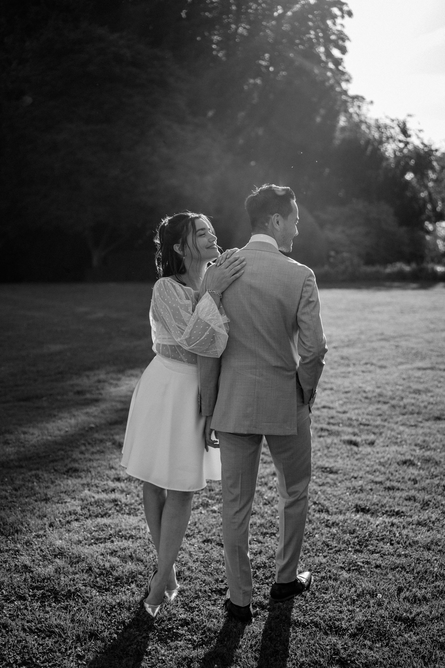 A couple walking together across a sunlit grassy field in black and white.