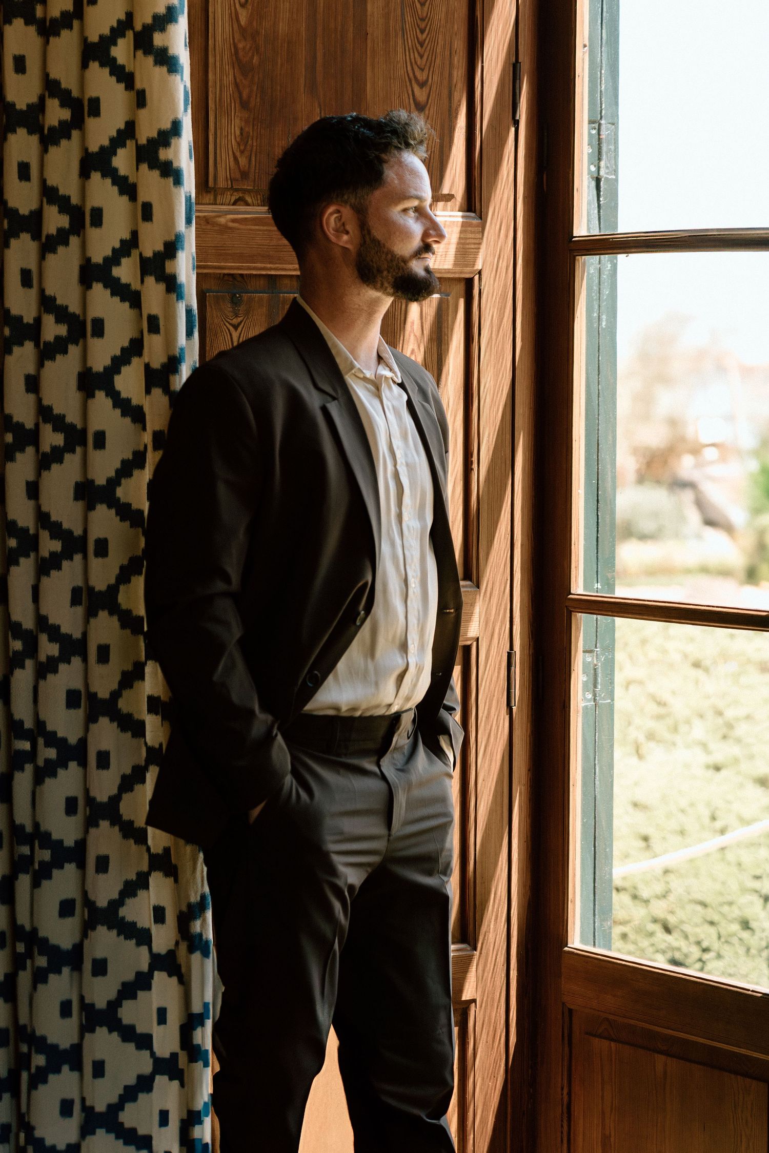 Person in formal attire gazes thoughtfully through a window in a wood-paneled room.