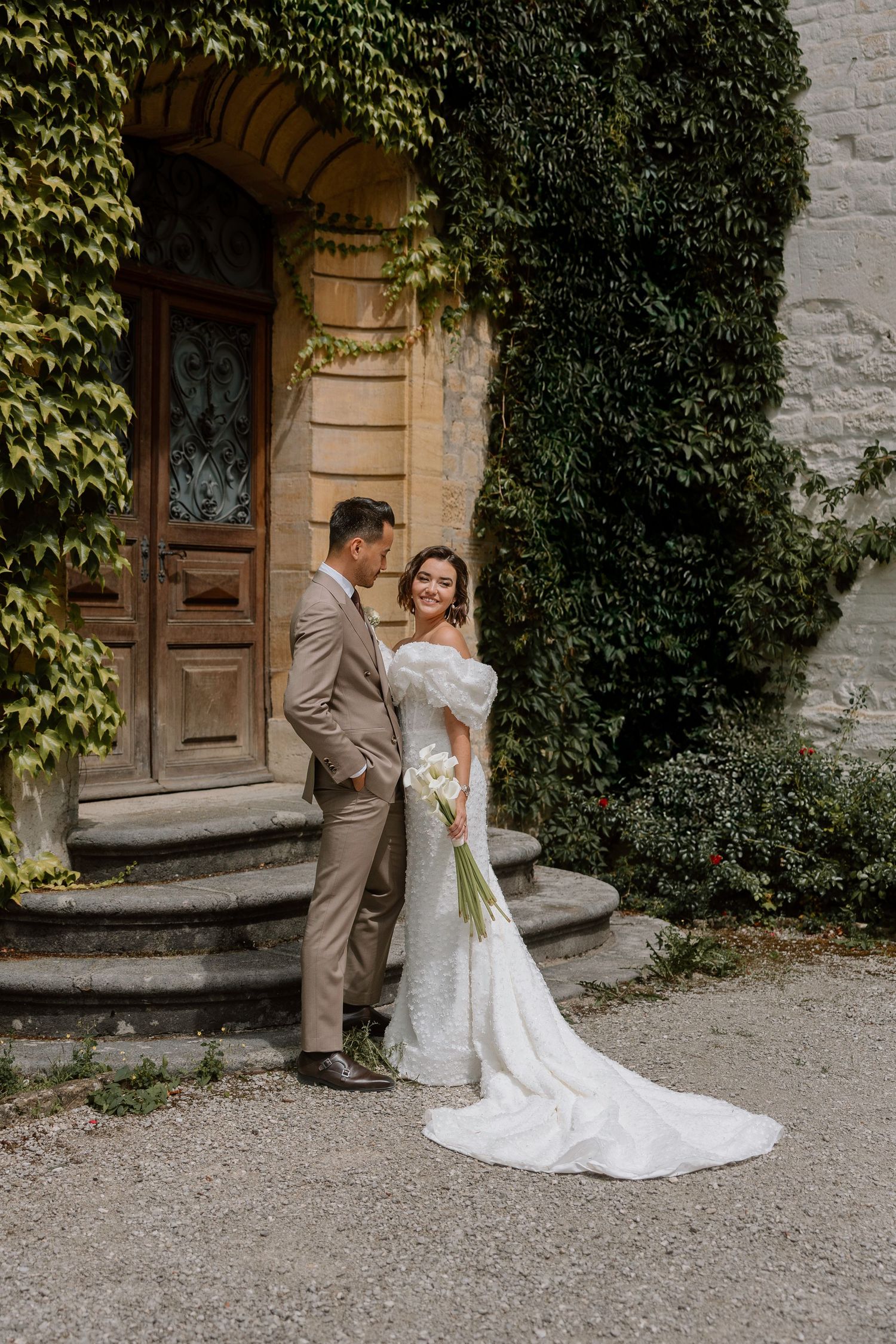 Romantic wedding couple poses and dances in front of an ivy-covered historic building entrance.
