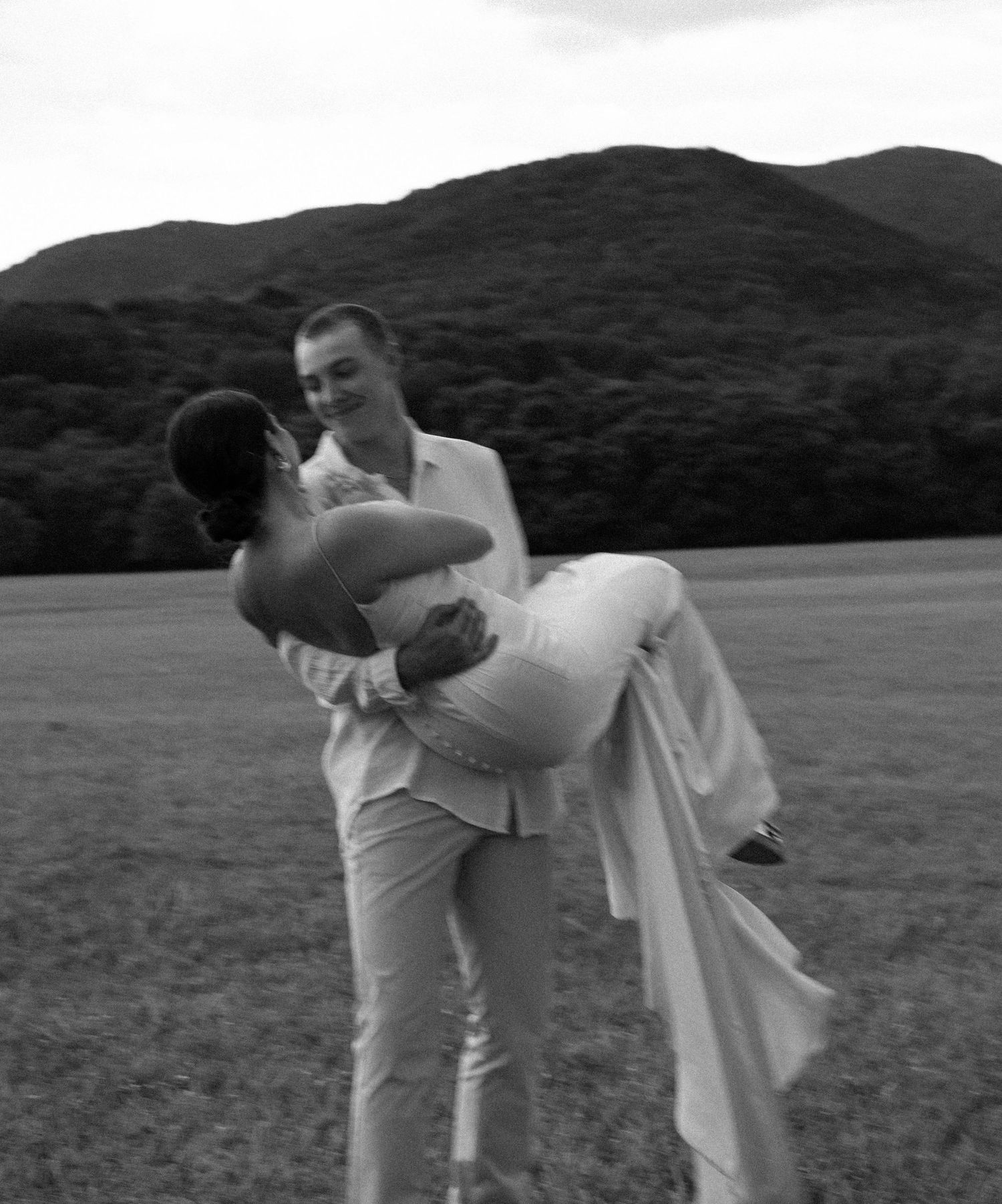 Black and white photo of a couple sharing intimate moments in a scenic mountain landscape.