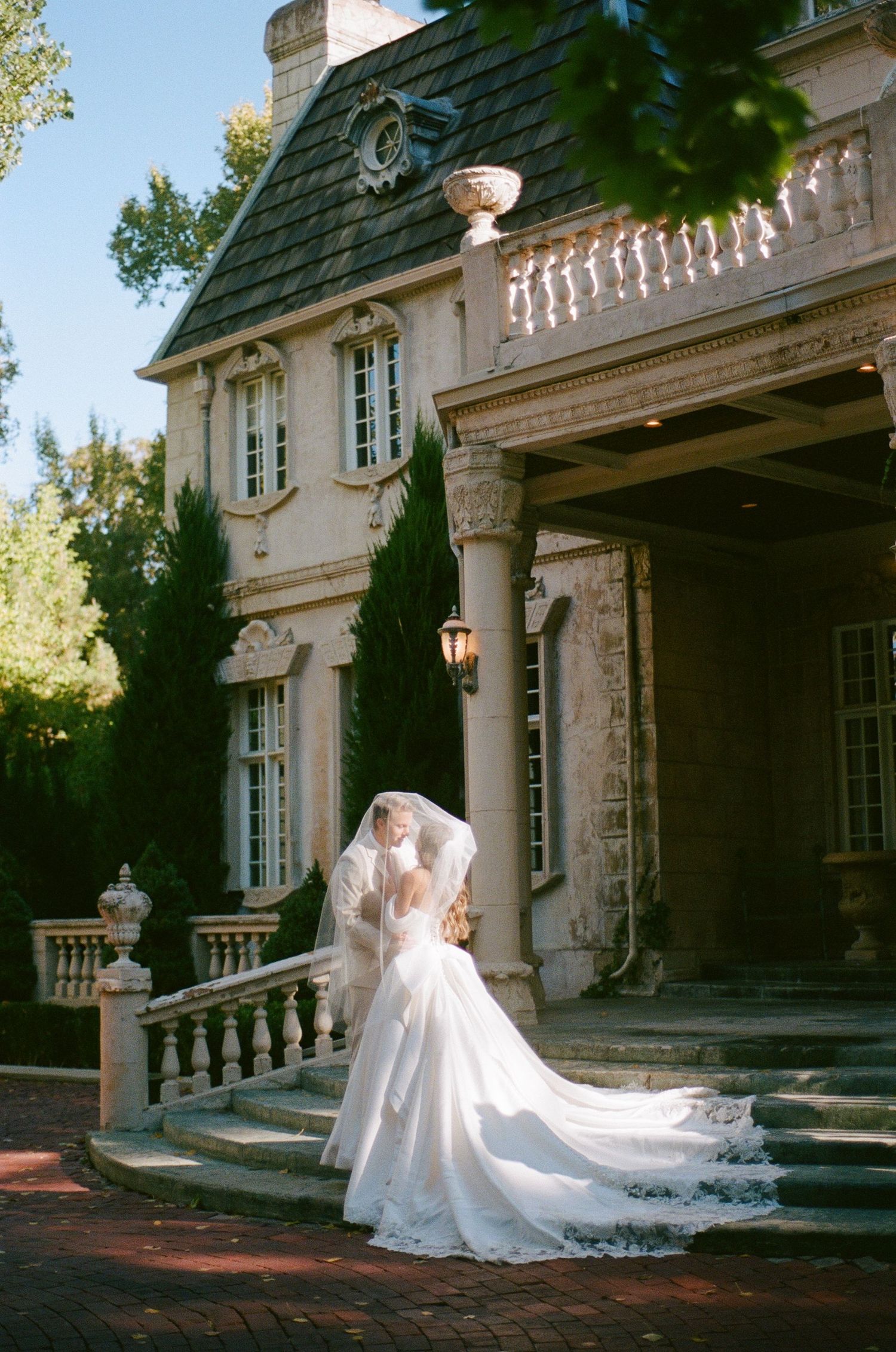 Dramatic wedding dress train flowing on steps of a grand stone mansion.