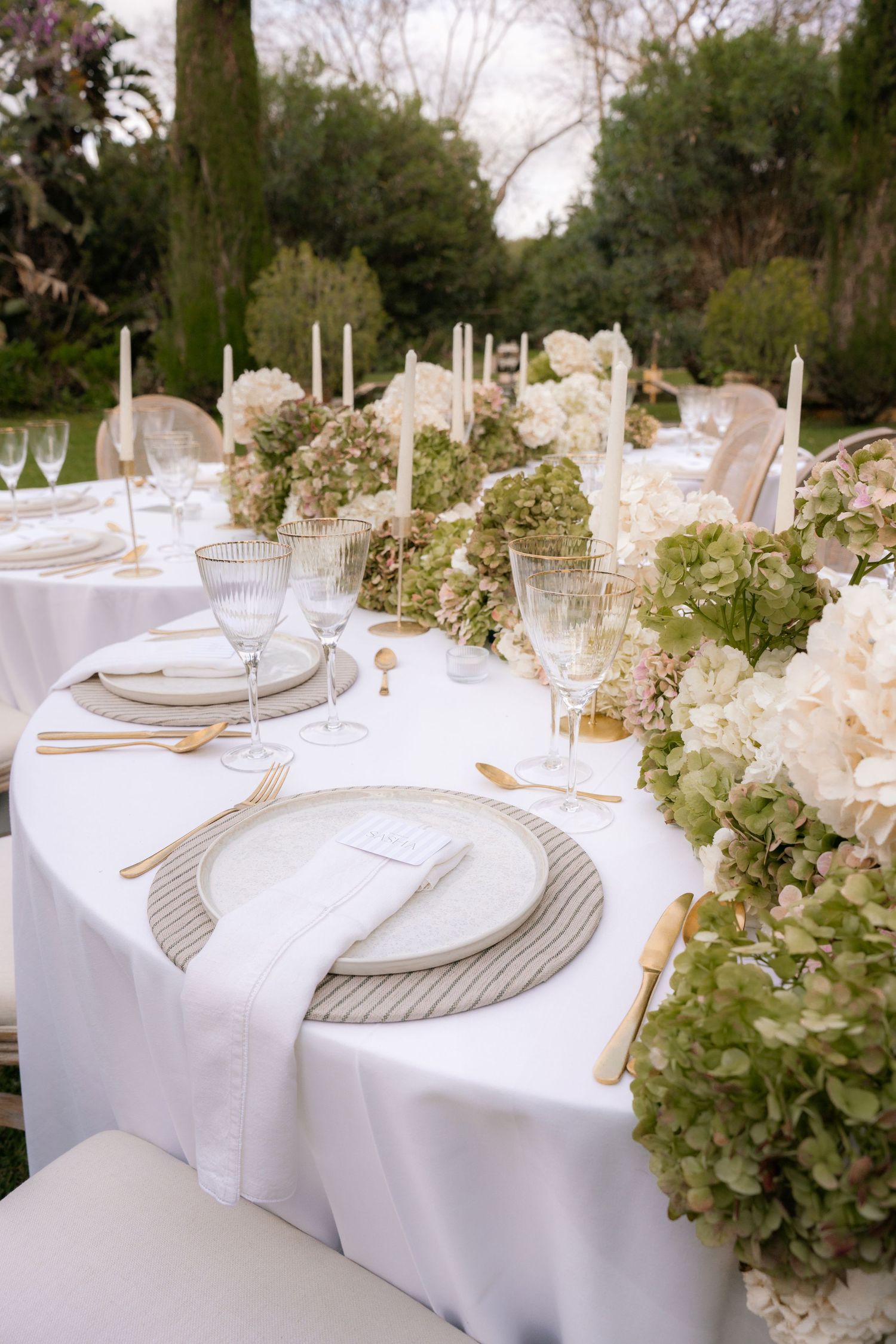 An elegant outdoor wedding table setting with white linens, crystal glasses and floral centerpieces.