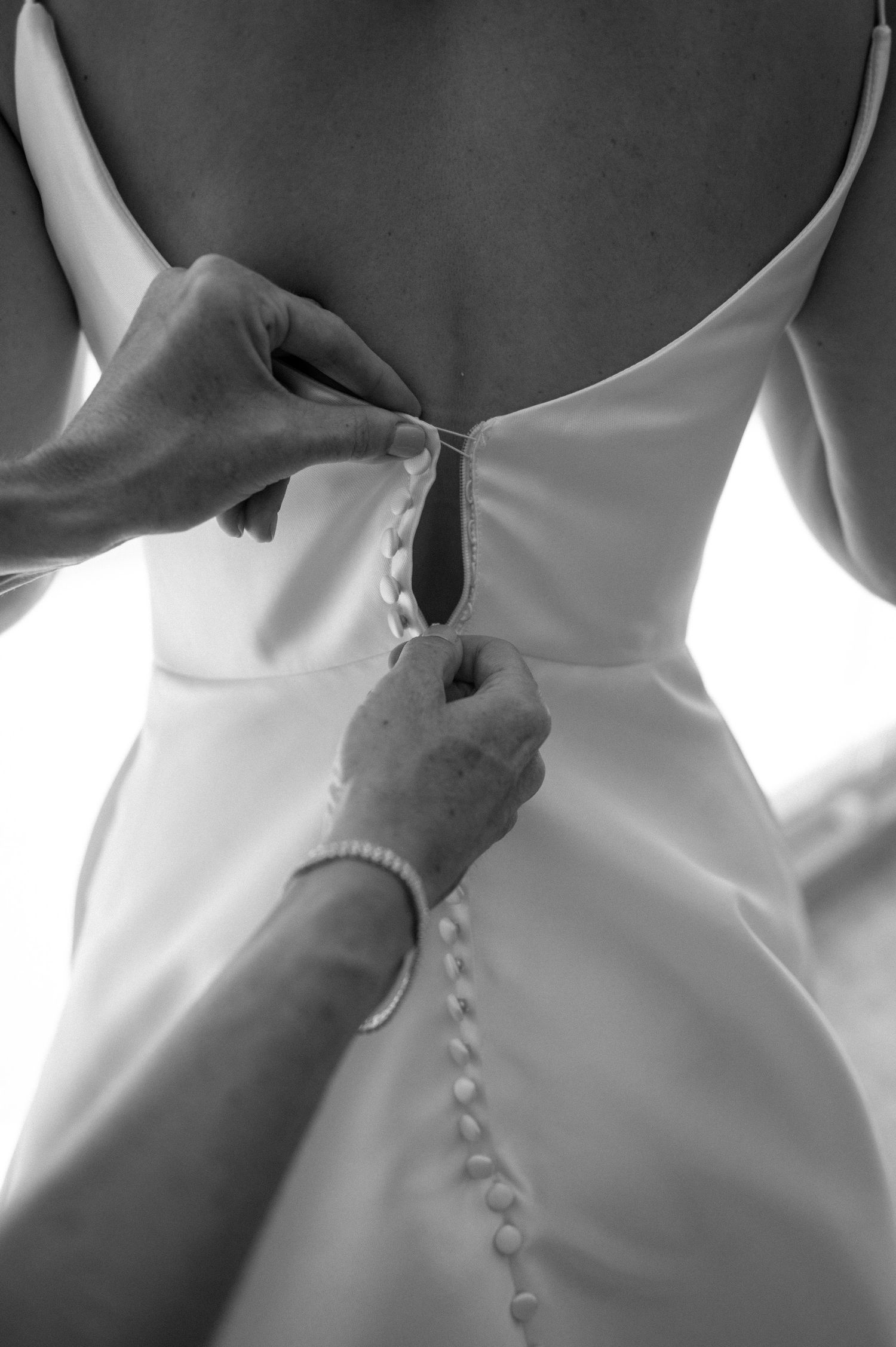 Black and white close-up of buttons being fastened on the back of a wedding dress.