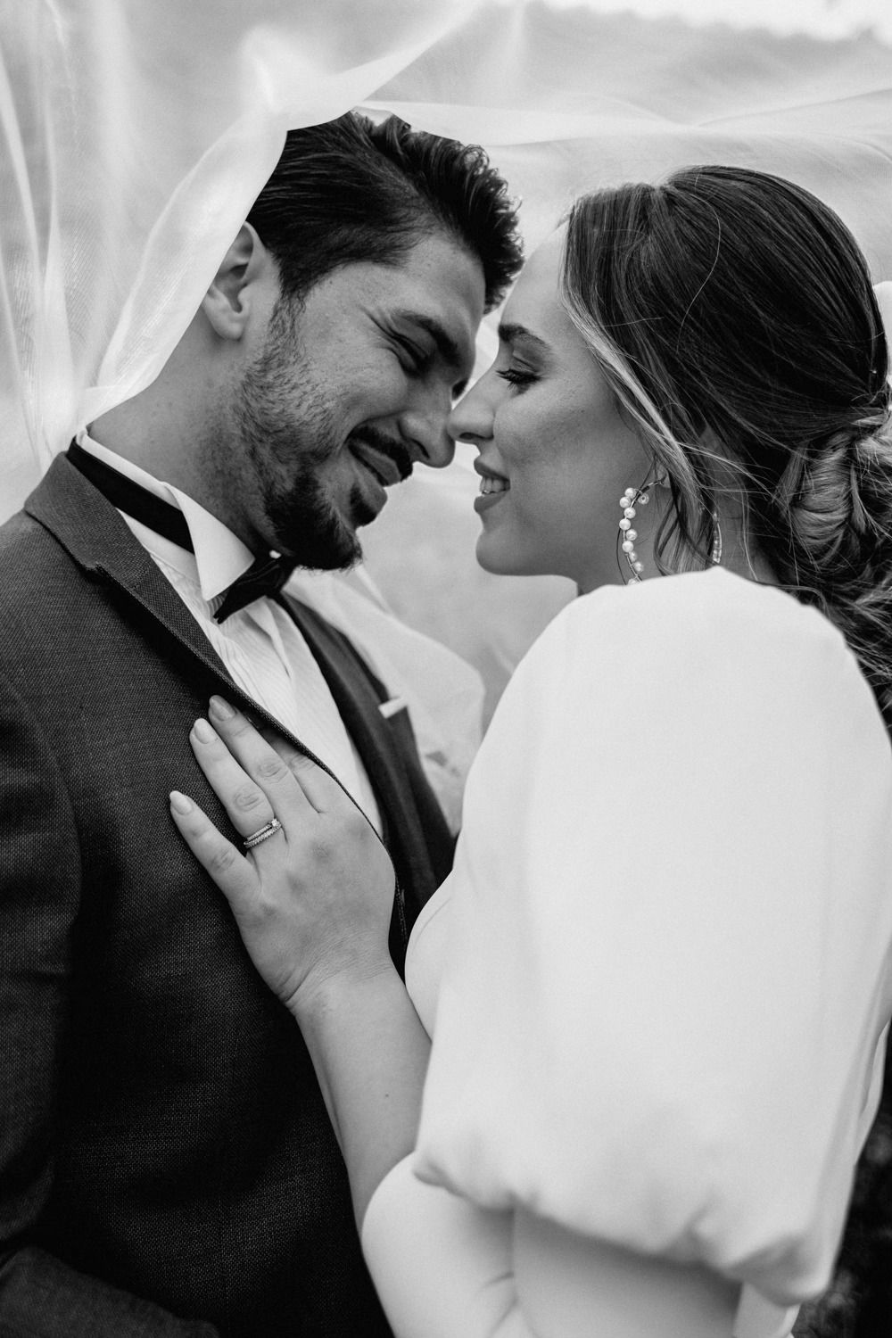 A tender black and white wedding moment captured under flowing white veil.