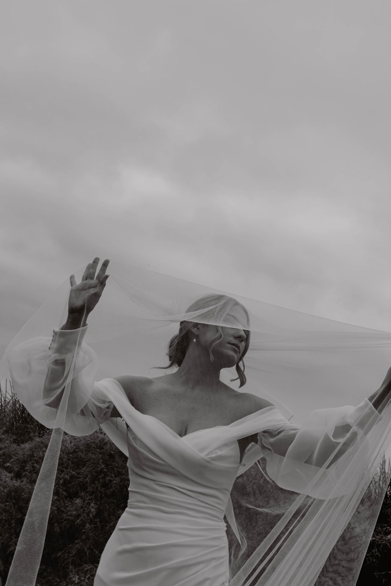 Artistic black and white photo of flowing white fabric against cloudy sky.