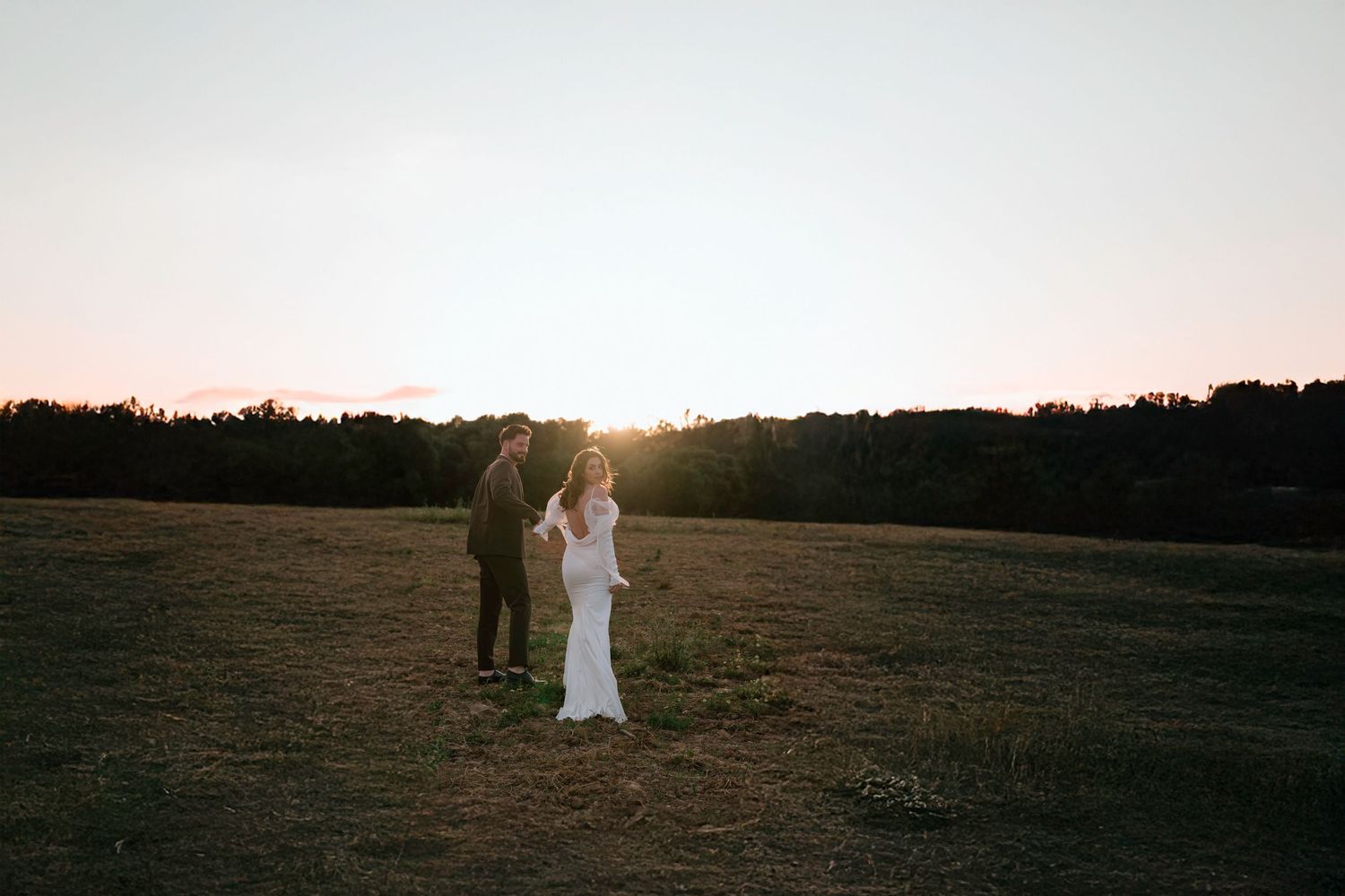 Wedding couple silhouetted against sunset in an open field.