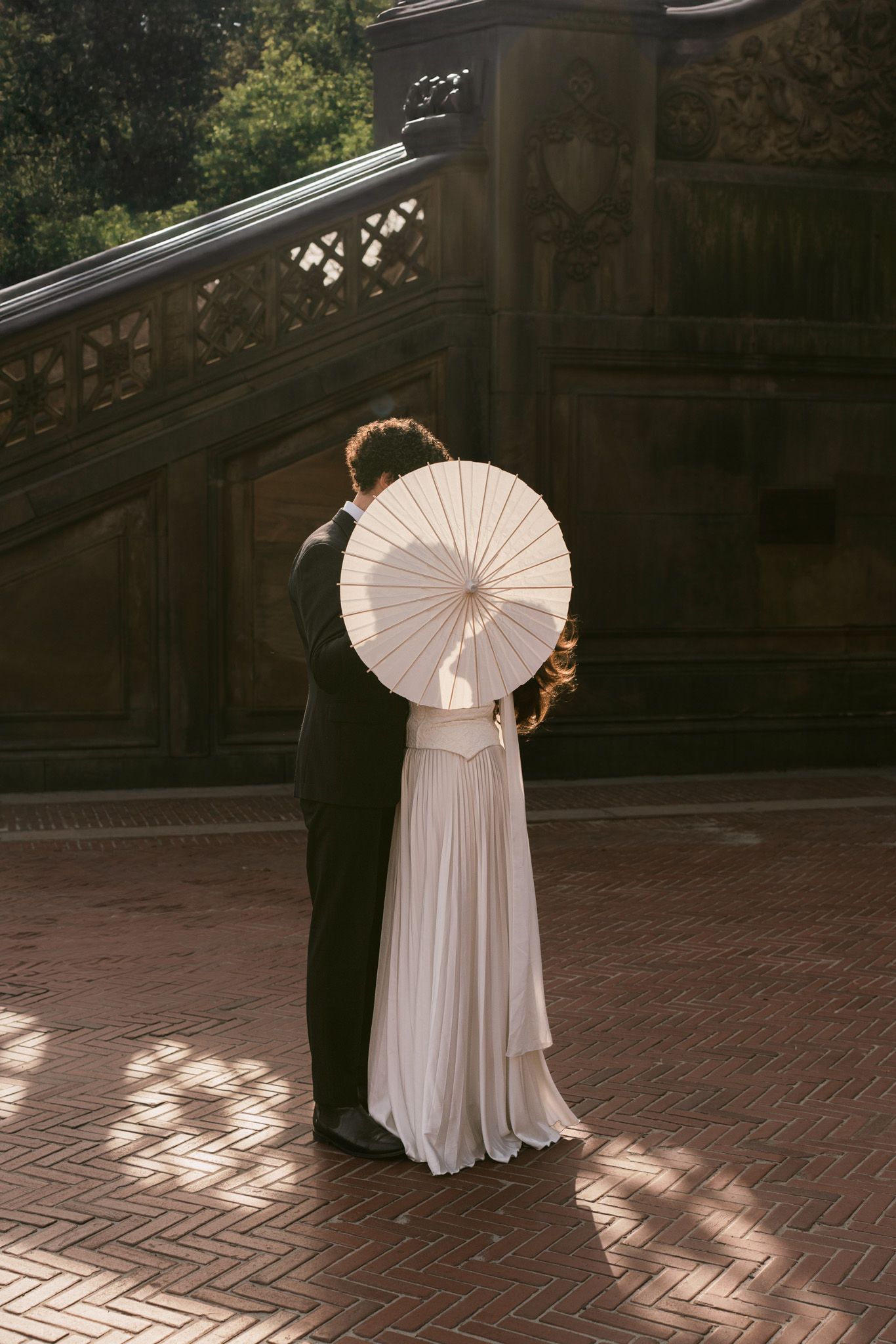 Silhouettes of a wedding couple dance on a sunny terrace with a white parasol.