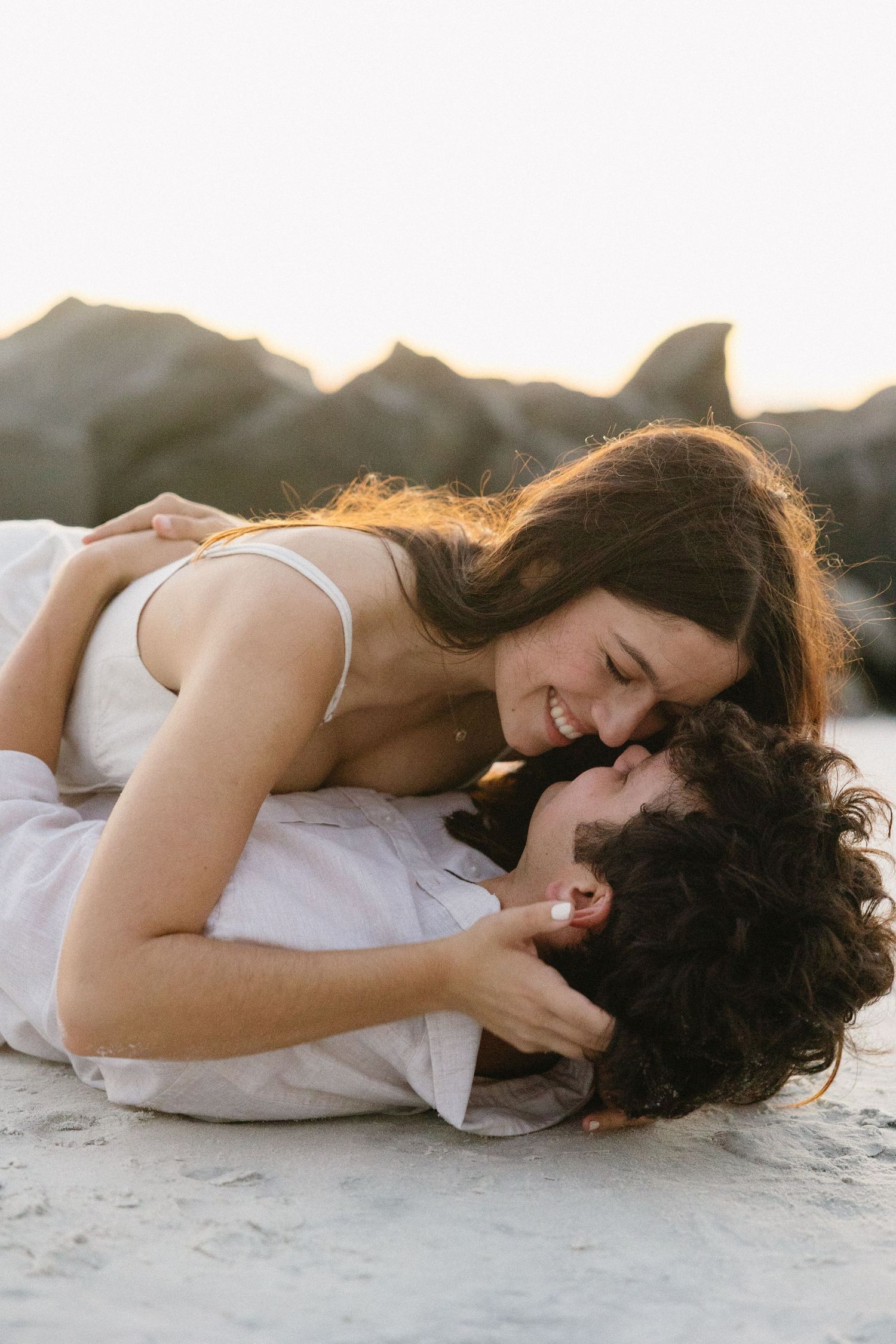 Romantic couple lying on beach sand during golden hour sharing intimate moments together.