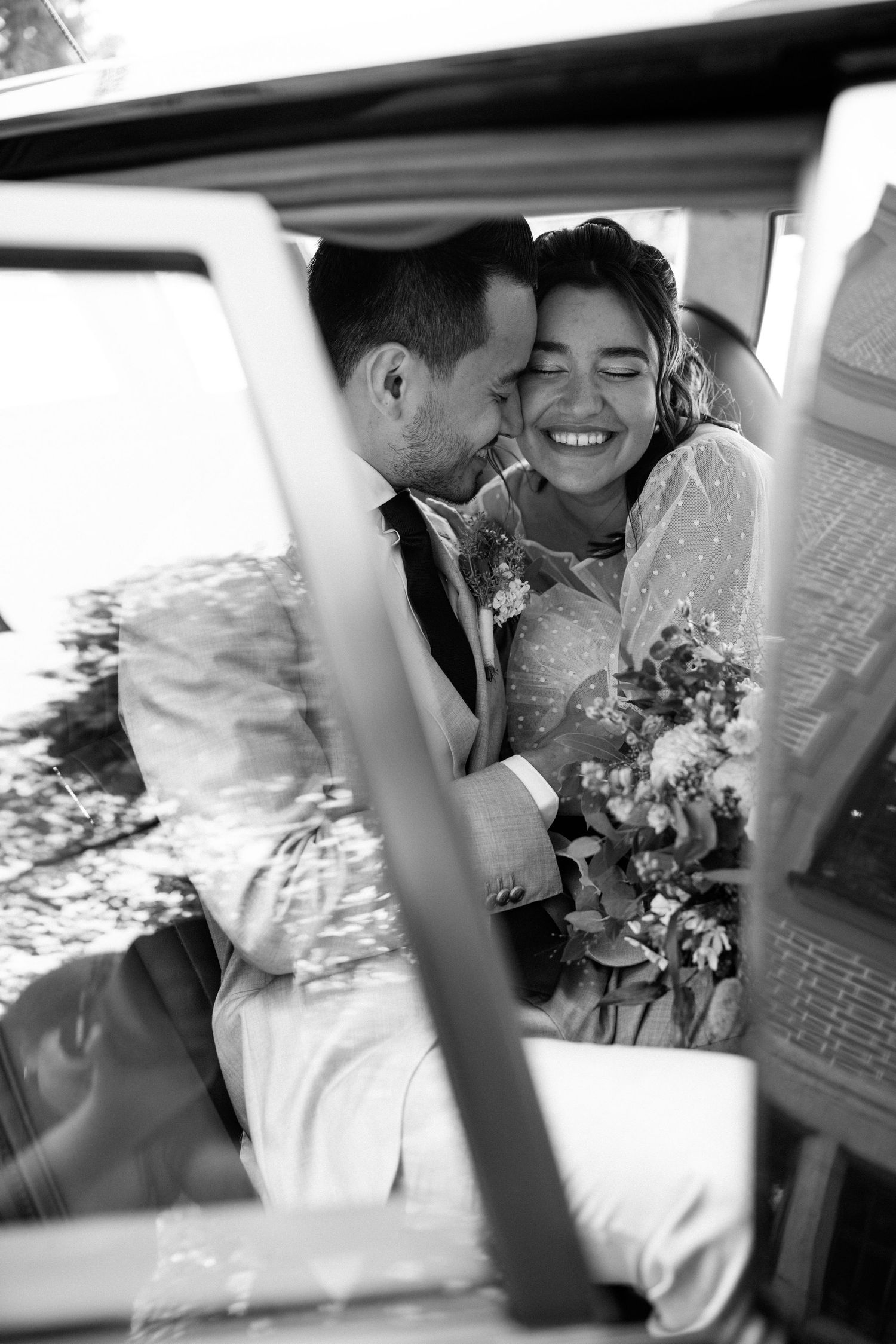 A couple sharing tender moments in a vintage car with wedding flowers.