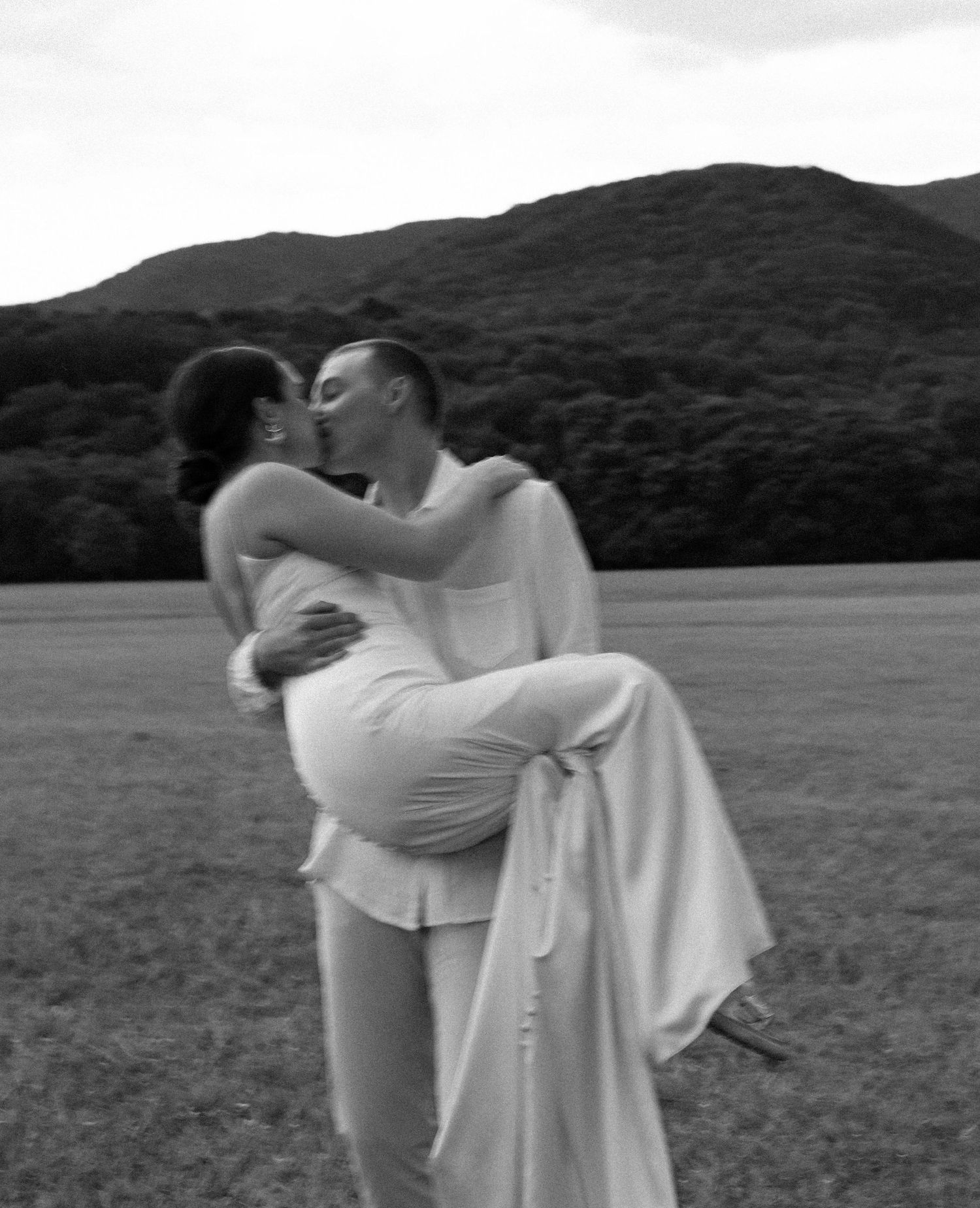 Couple in white sharing tender moments against a mountain landscape backdrop.