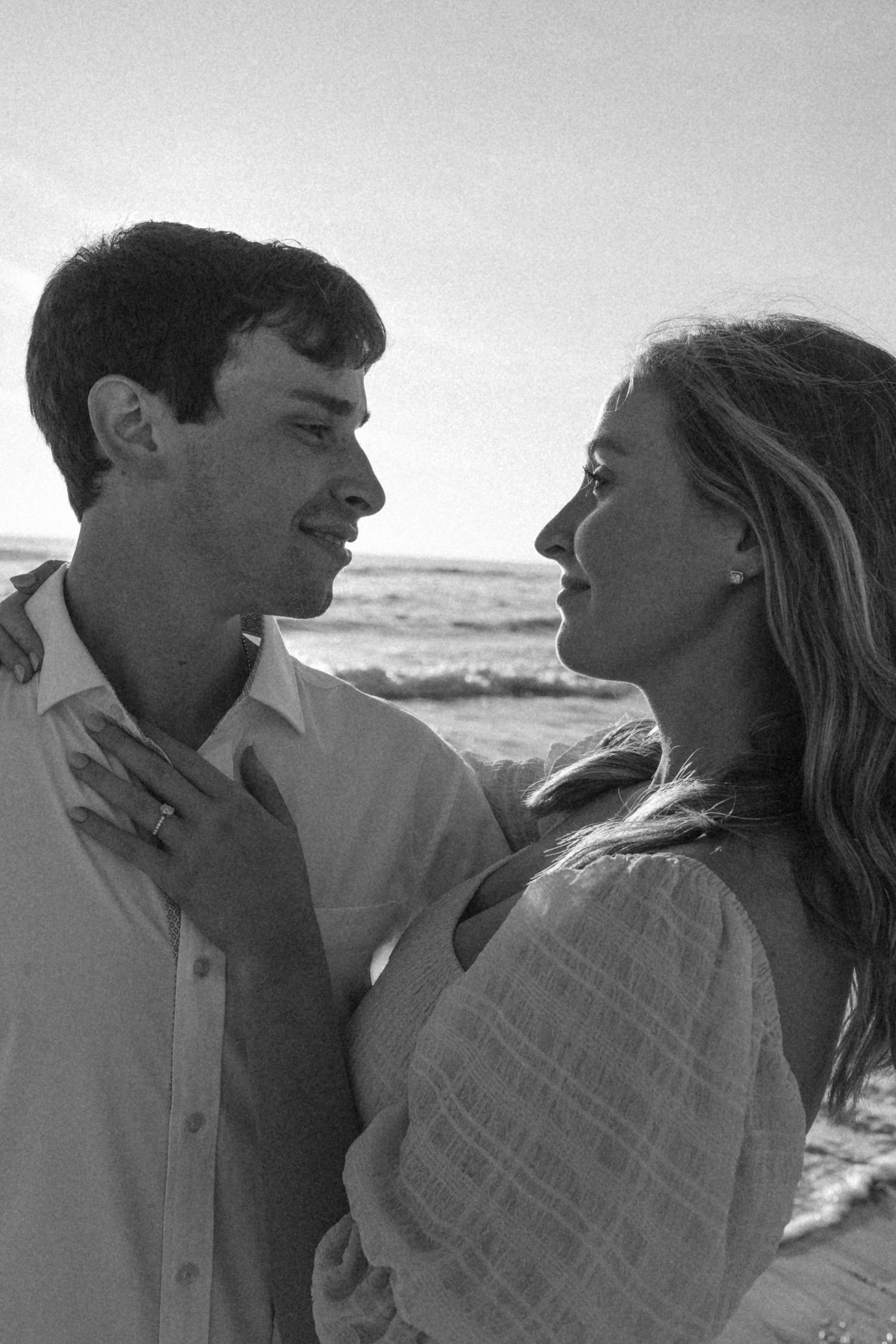 Black and white beach portraits of couple sharing affectionate moments by the ocean.