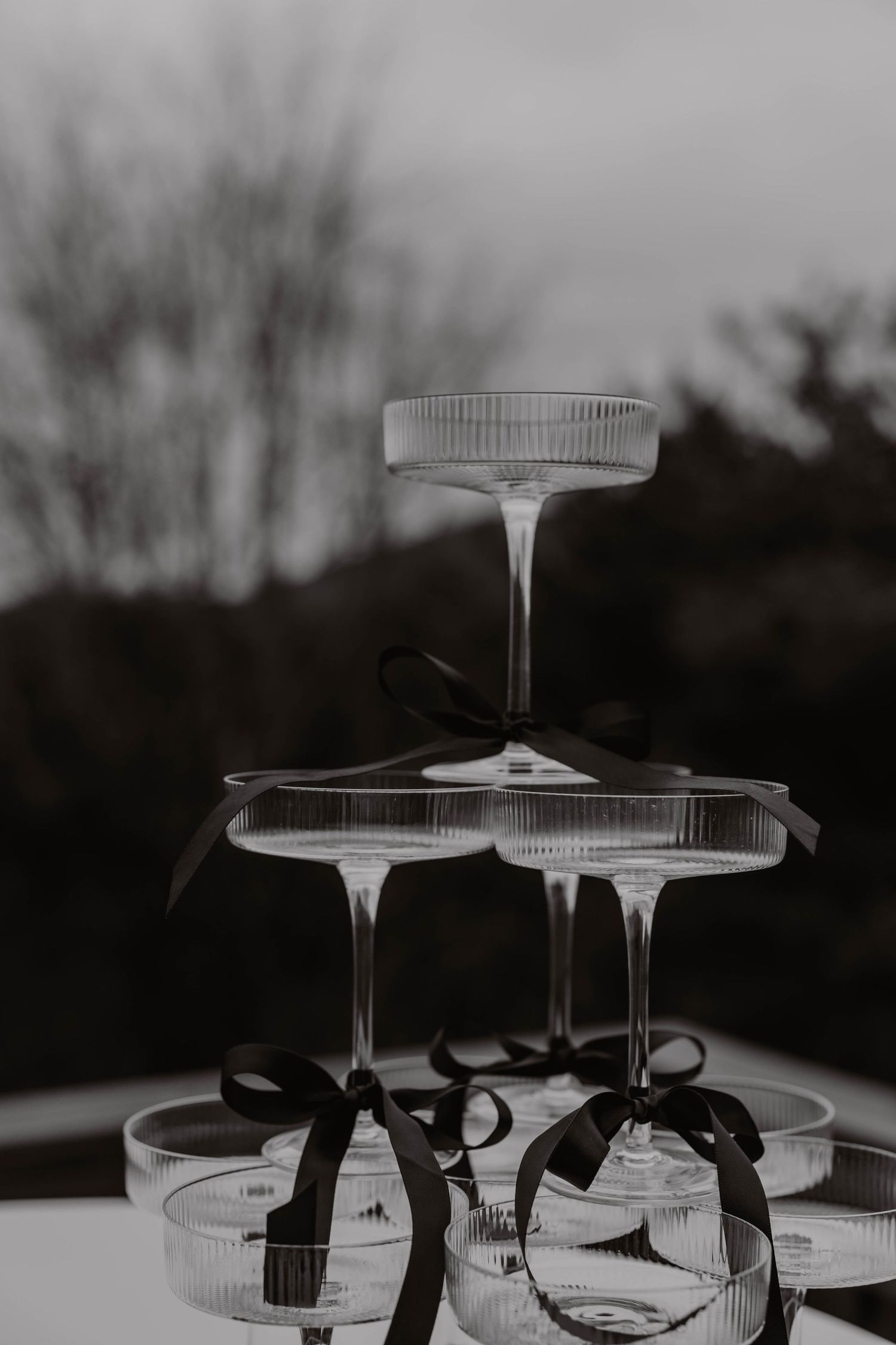 Champagne glasses stacked in tower with black ribbons for wedding celebration.
