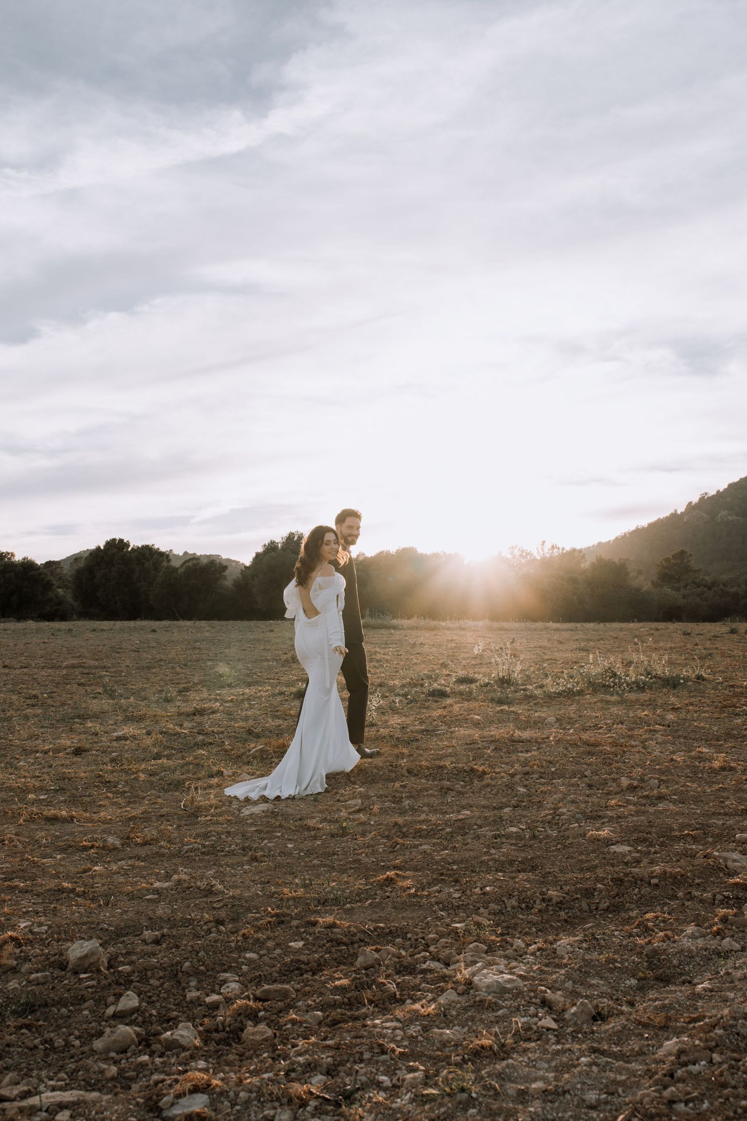 A couple poses in a golden sunset on a rustic hill overlooking mountain landscapes.