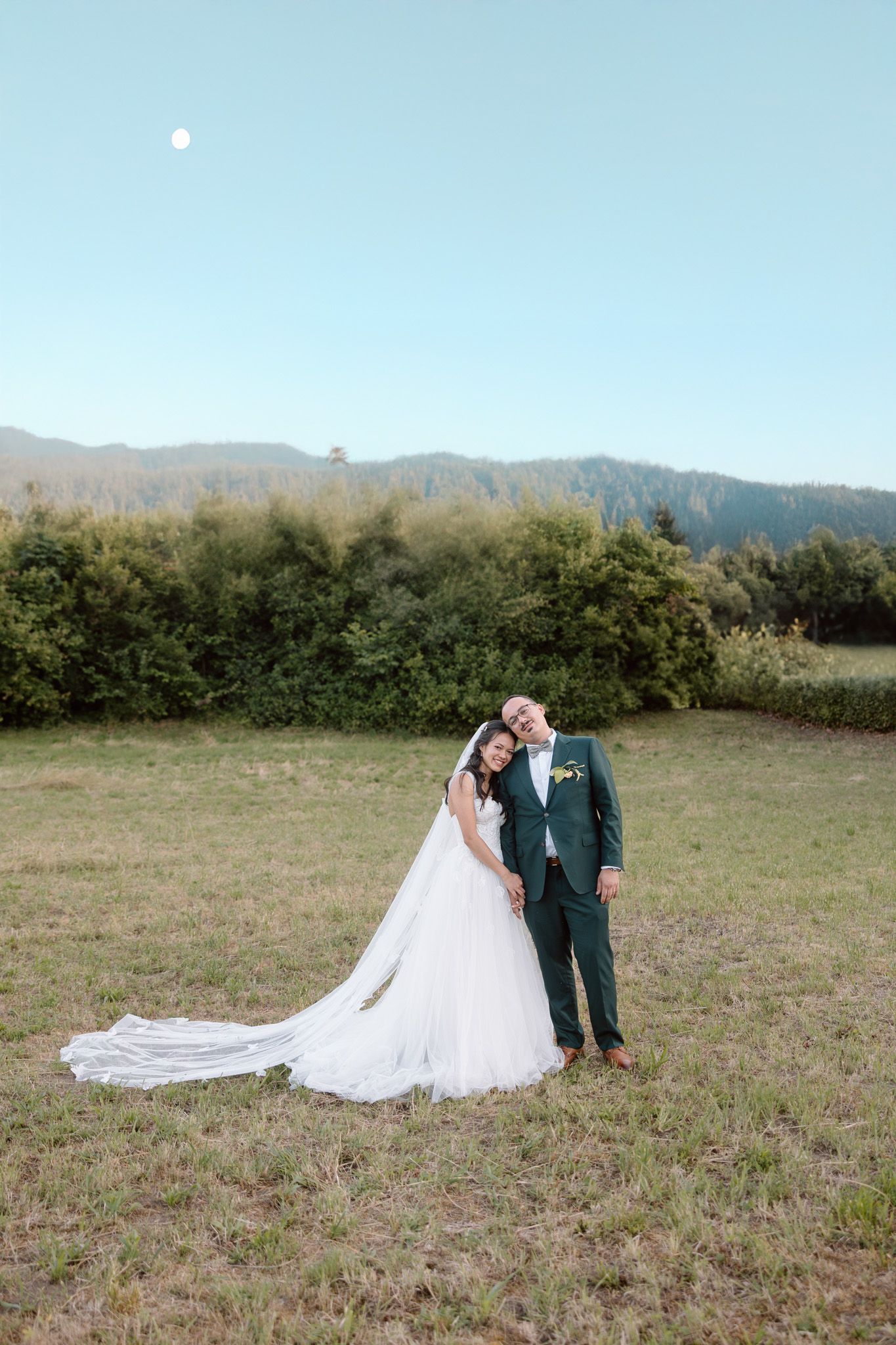 Wedding couple embracing in a mountain meadow with a flowing white dress train.