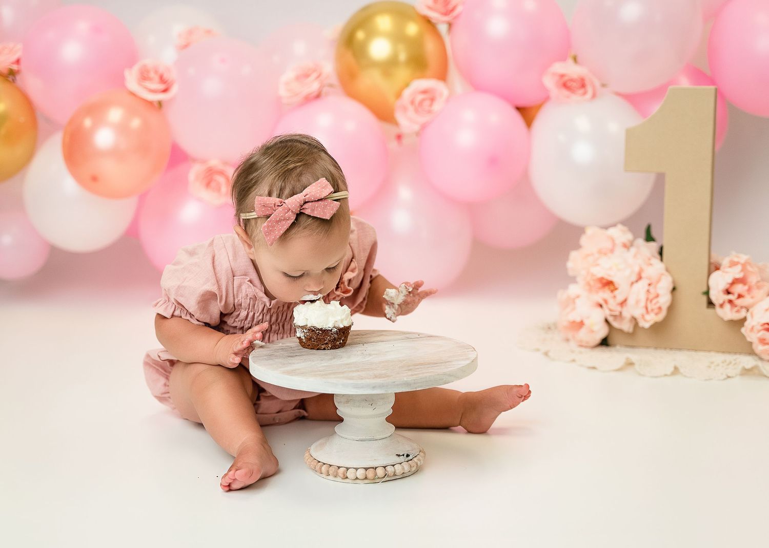First birthday celebration with cupcake and pink balloon arch backdrop.