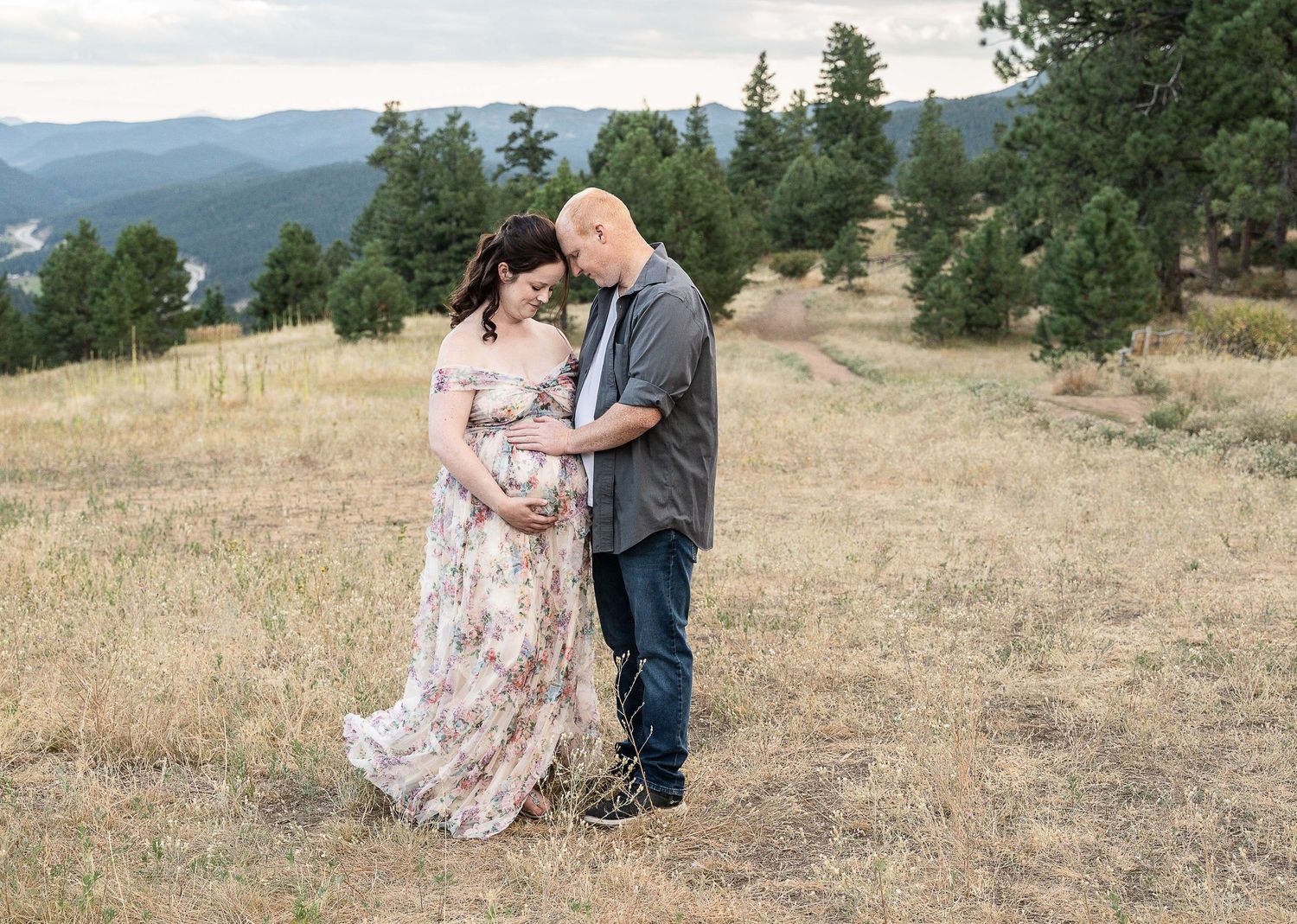 A couple shares an intimate moment together on a grassy hillside with mountain views in the background.
