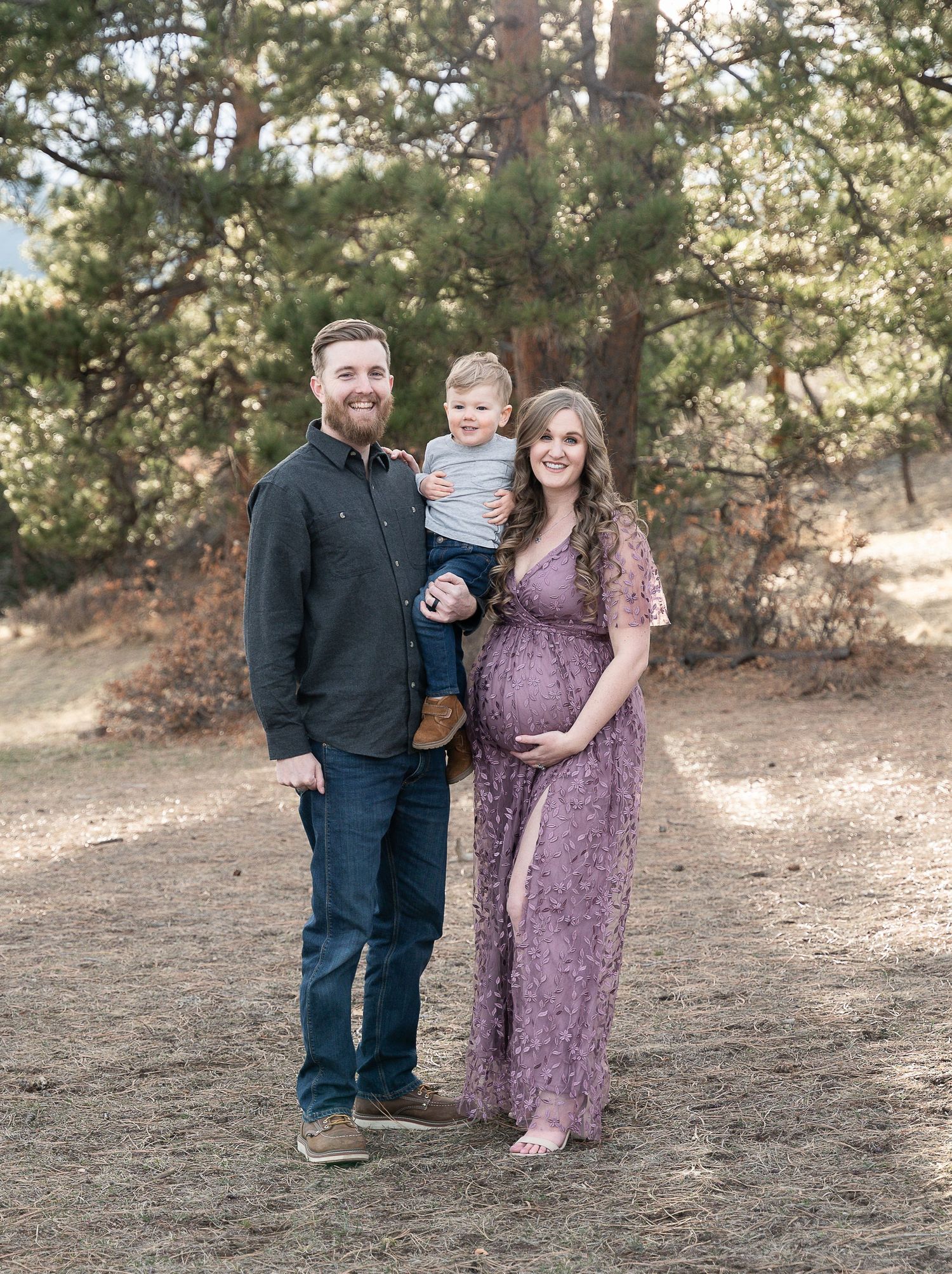 A family poses outdoors in a wooded setting with pine trees in the background.