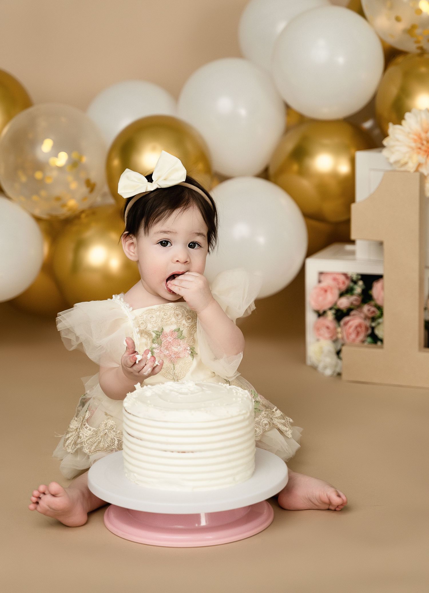 Elegant cake smash setup with gold and white balloons and floral decorations.