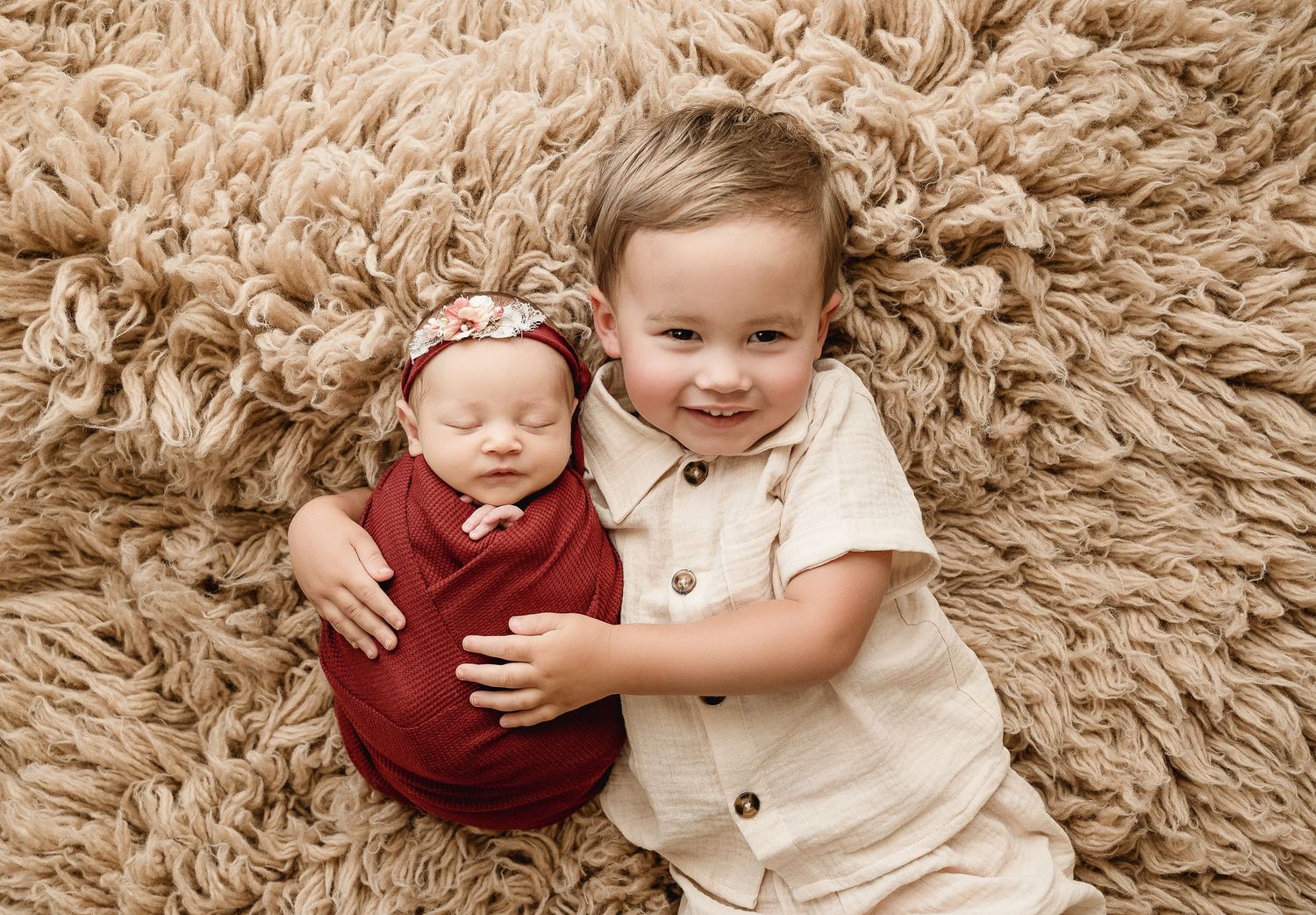 Young children laying on plush beige carpet during tender portrait session.