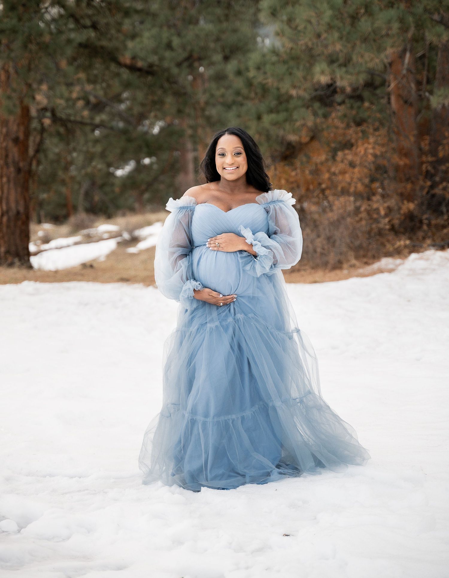 Winter maternity portrait featuring a light blue tulle gown in snowy mountain setting.