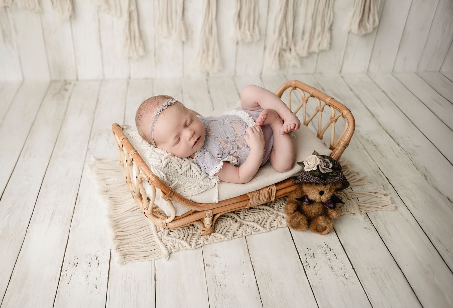 A newborn baby lying on a wooden floor in a natural-toned studio setting with neutral colors and textures.