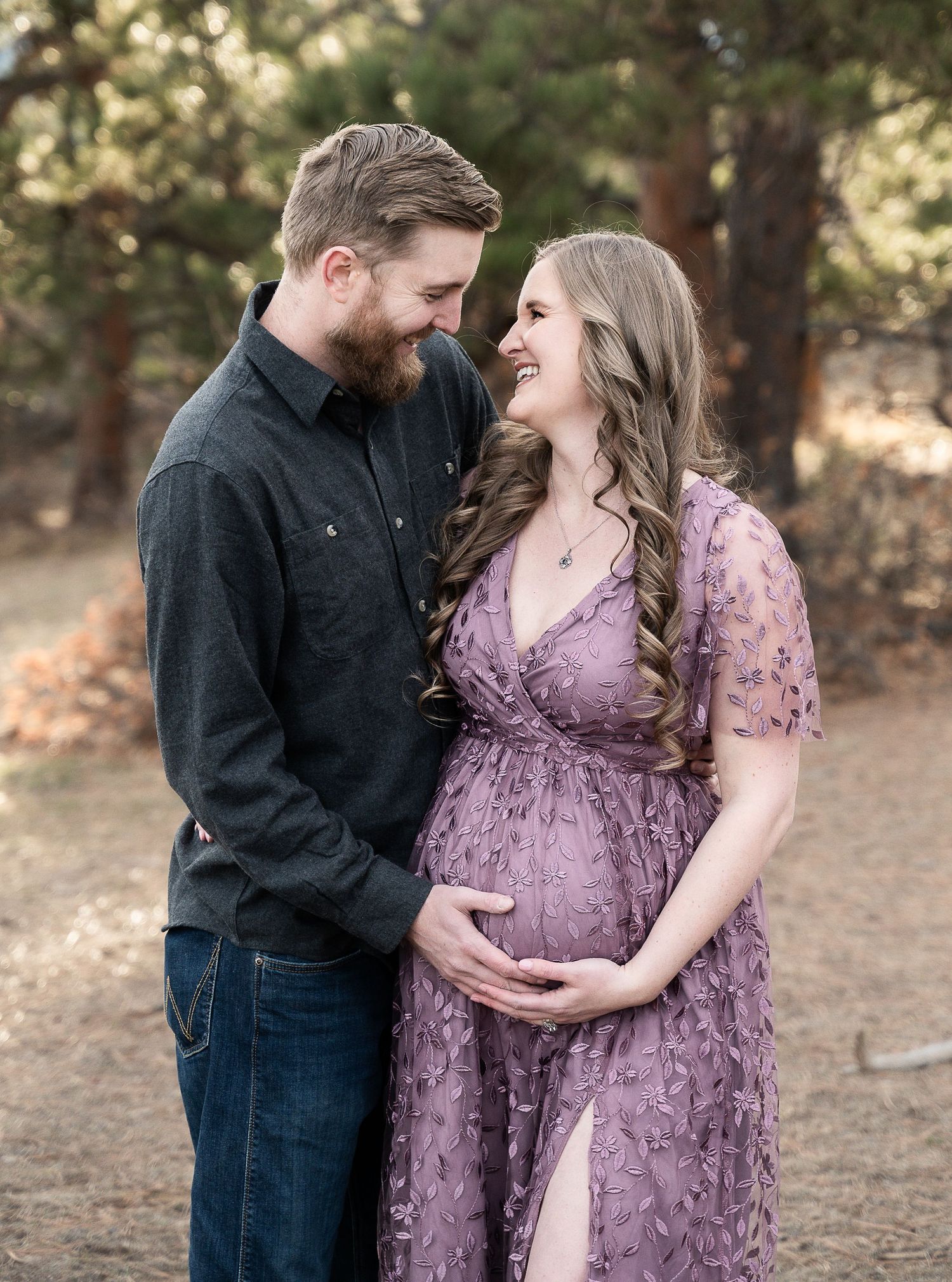 A romantic maternity photo shows a couple embracing in a forest setting.