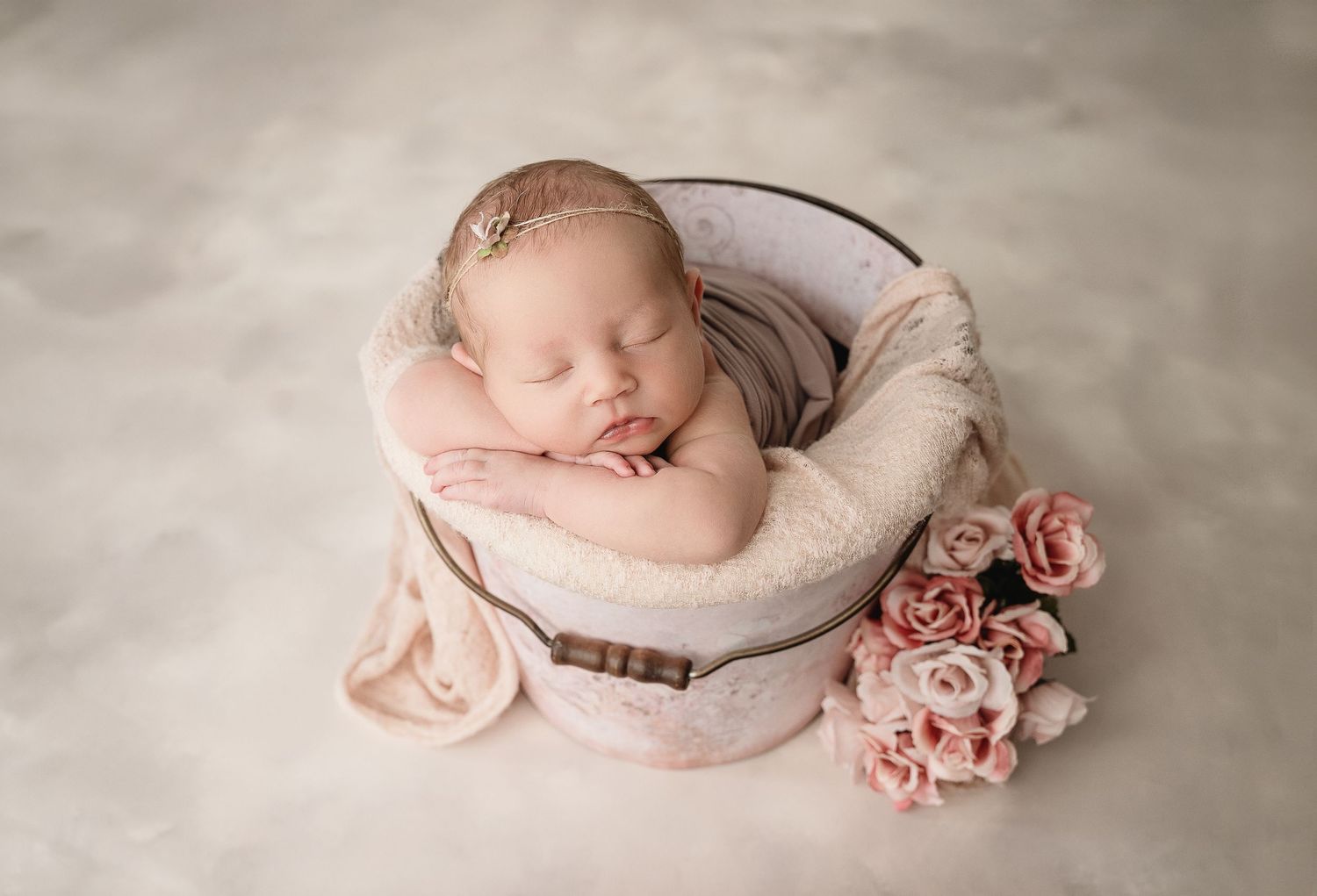 A delicate newborn baby sleeping peacefully in a pink blanket with soft rose decorations in muted tones.