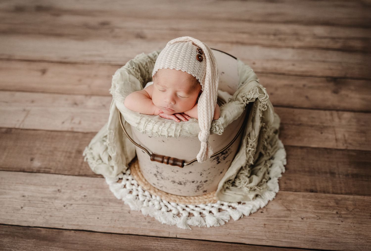Sleeping newborn nestled in cozy beige basket with lace trim on rustic wooden floor.
