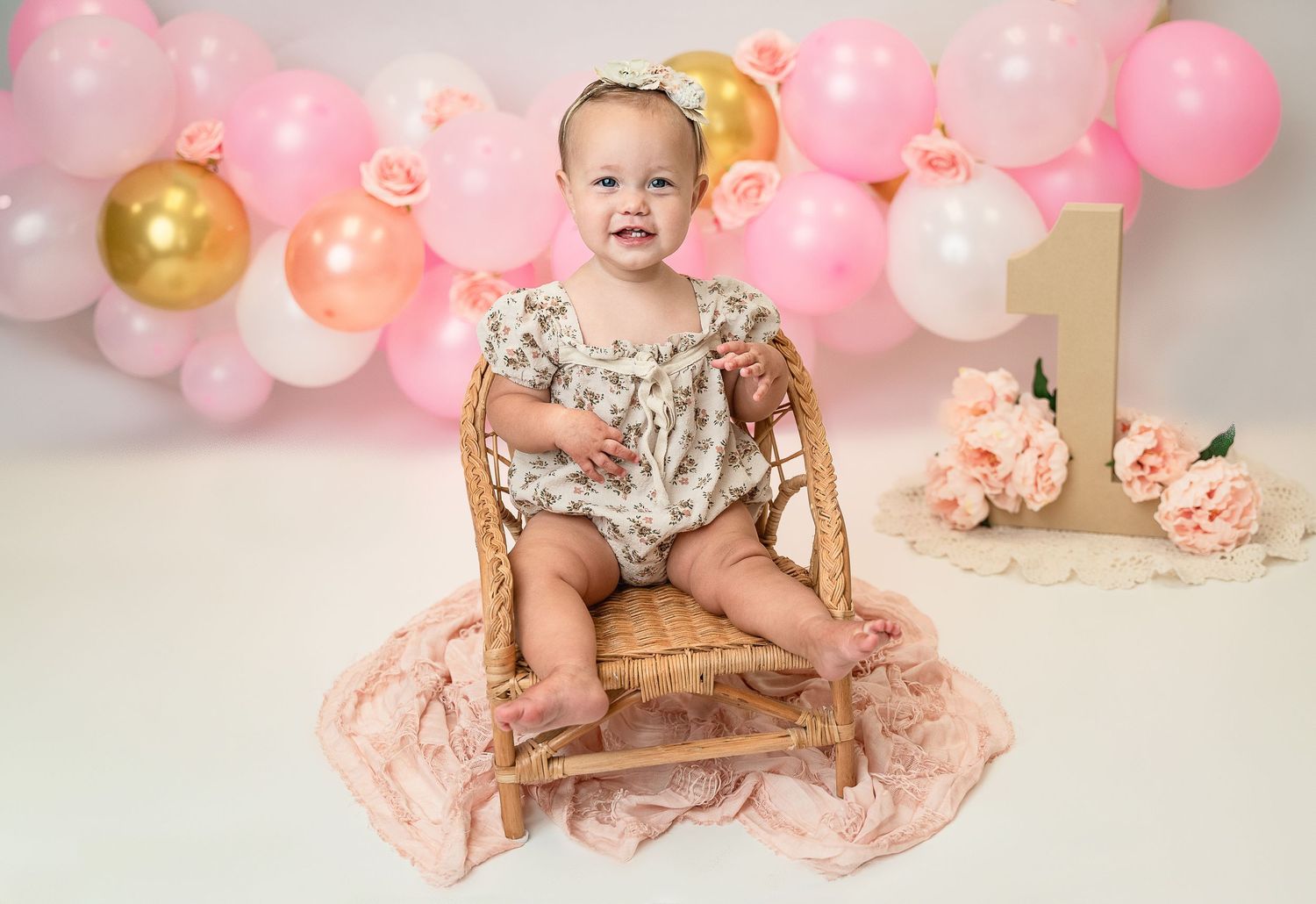 Pink and gold birthday setup with vintage chair and balloon arch decorations.