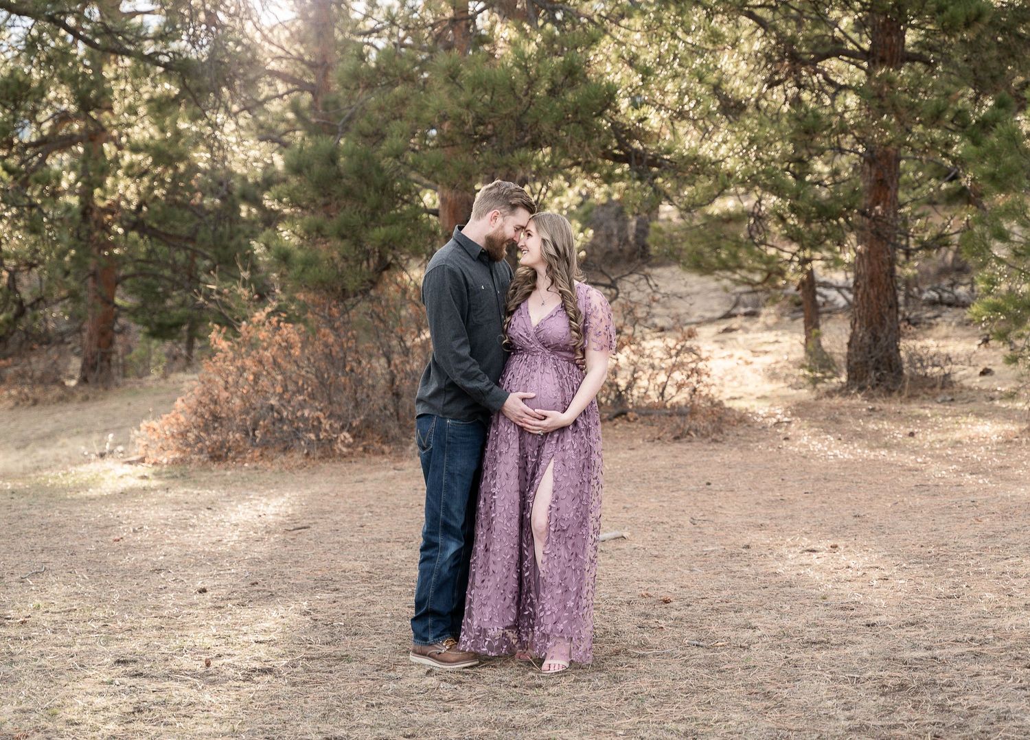 A romantic couple in matching shades of purple and navy walk and pose together in a sunlit forest setting.