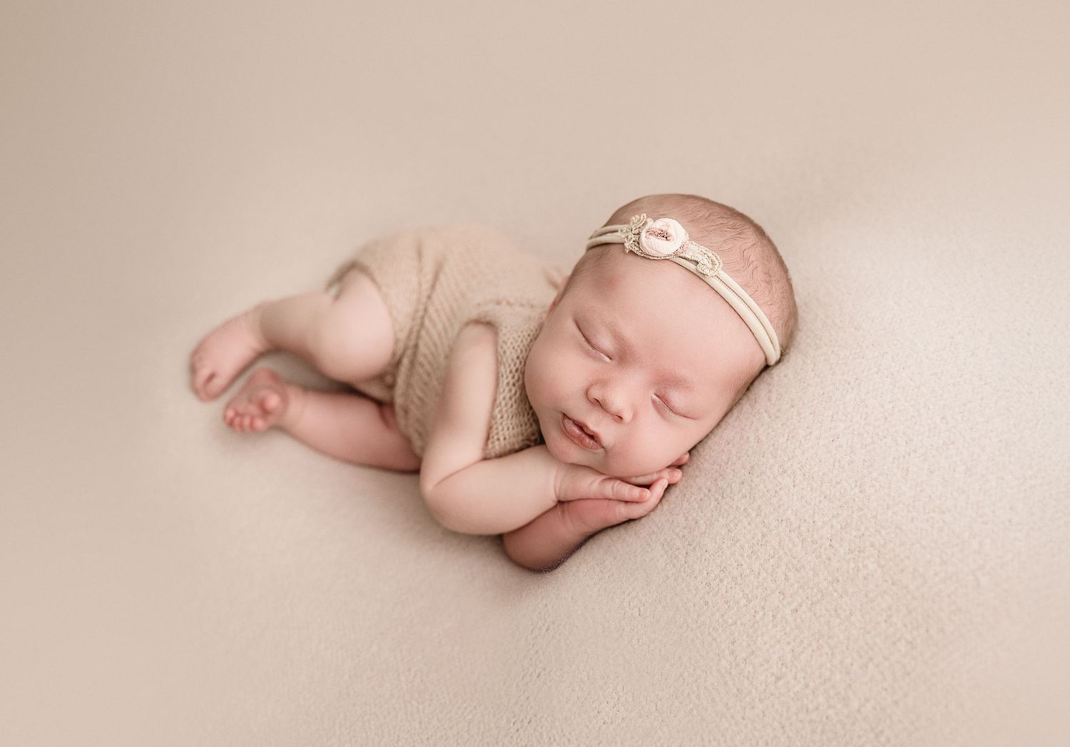 Sleeping newborn baby in neutral tones curled up in peaceful pose against soft beige background. Newborn photos in Denver Colorado
