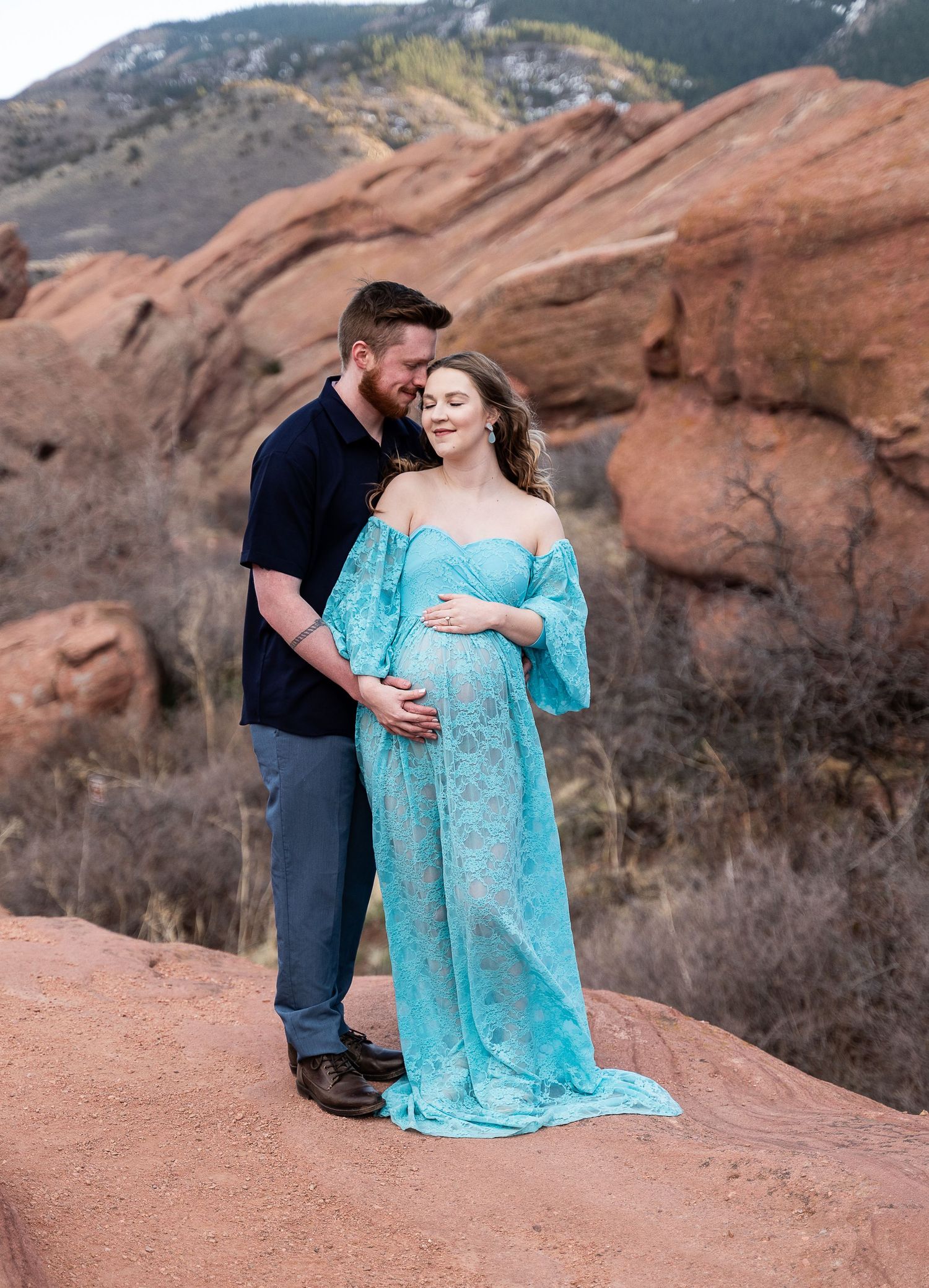 A couple embraces during their maternity photoshoot at a scenic red rock location.