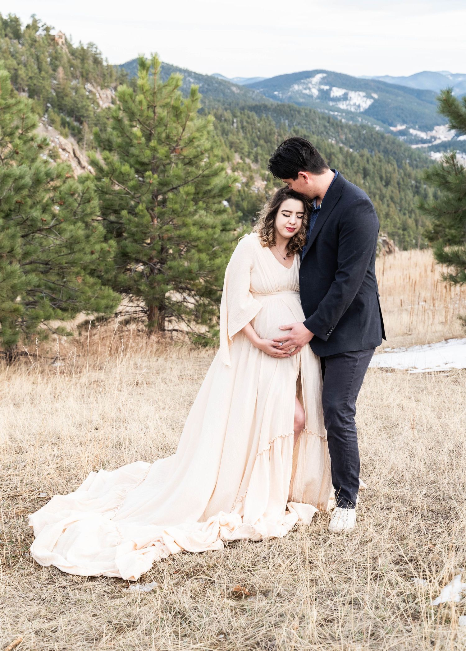 A romantic couple shares intimate moments in a mountainous winter landscape wearing formal attire and a blush gown.