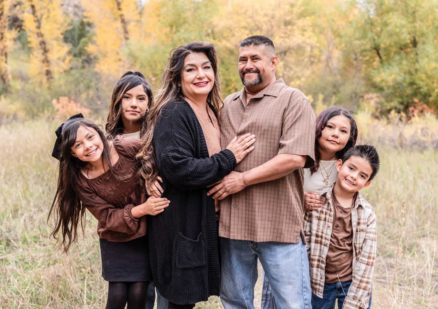 A family enjoys a candid moment together in a golden autumn field during an outdoor photo session.