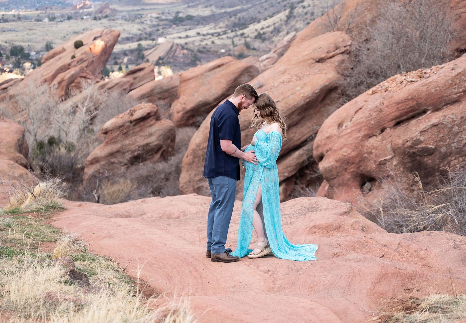 Couple embracing at scenic Red Rocks Park against dramatic mountain landscape and cloudy sky.