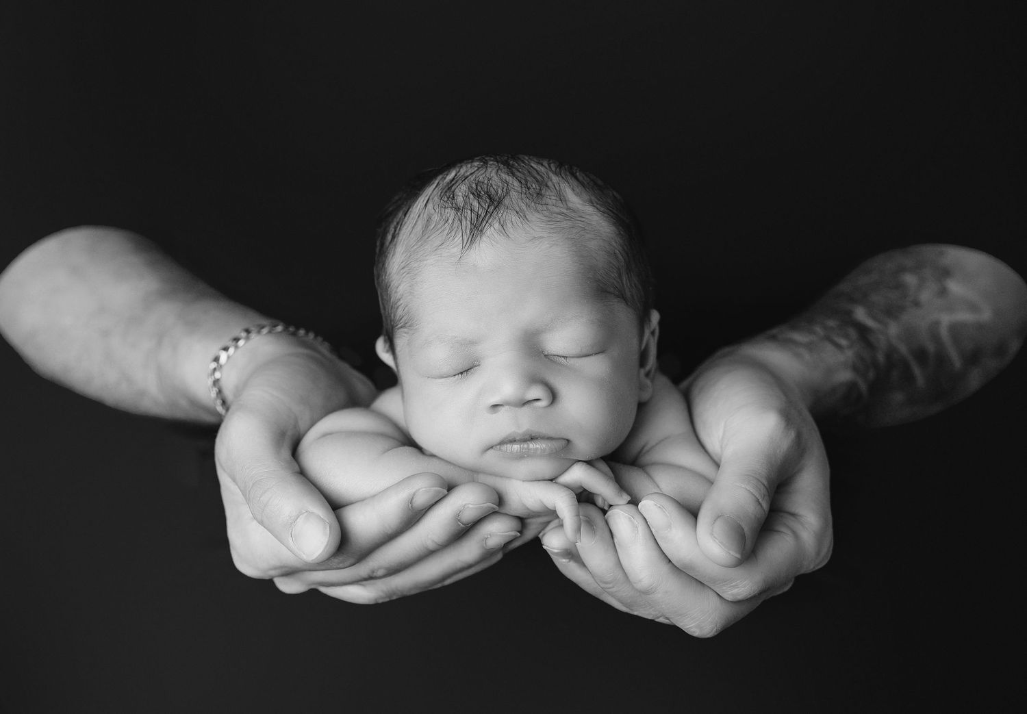 Black and white close-up photograph showing hands gently cradling a newborn baby.