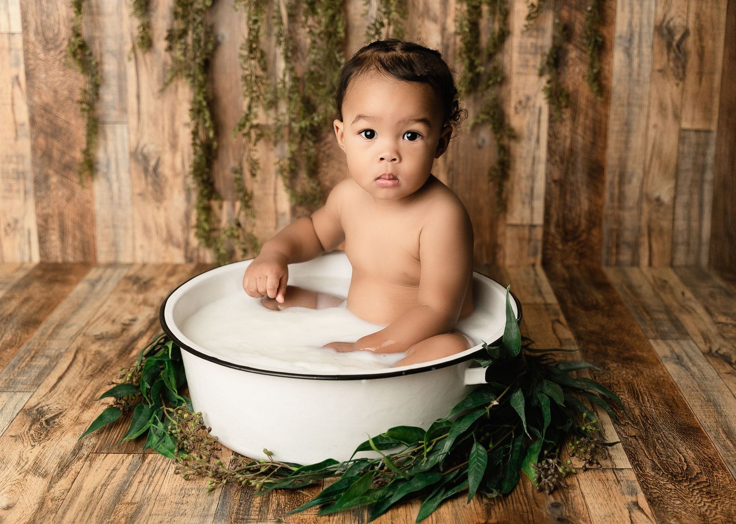 Rustic themed portrait with vintage enamel basin and pine greenery on wooden floor backdrop.