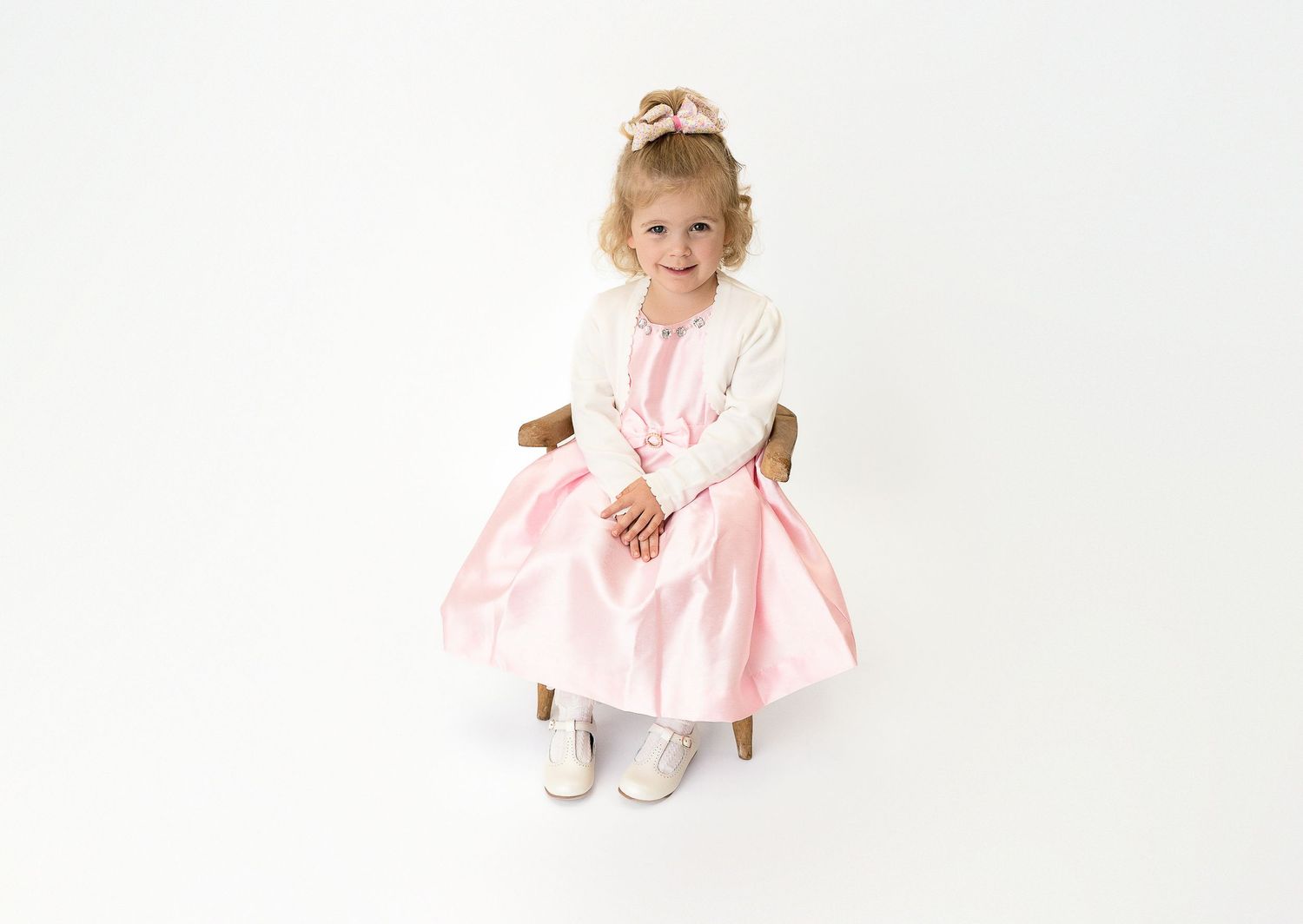 Sweet pink dress photoshoot with rustic wooden chair and white backdrop.