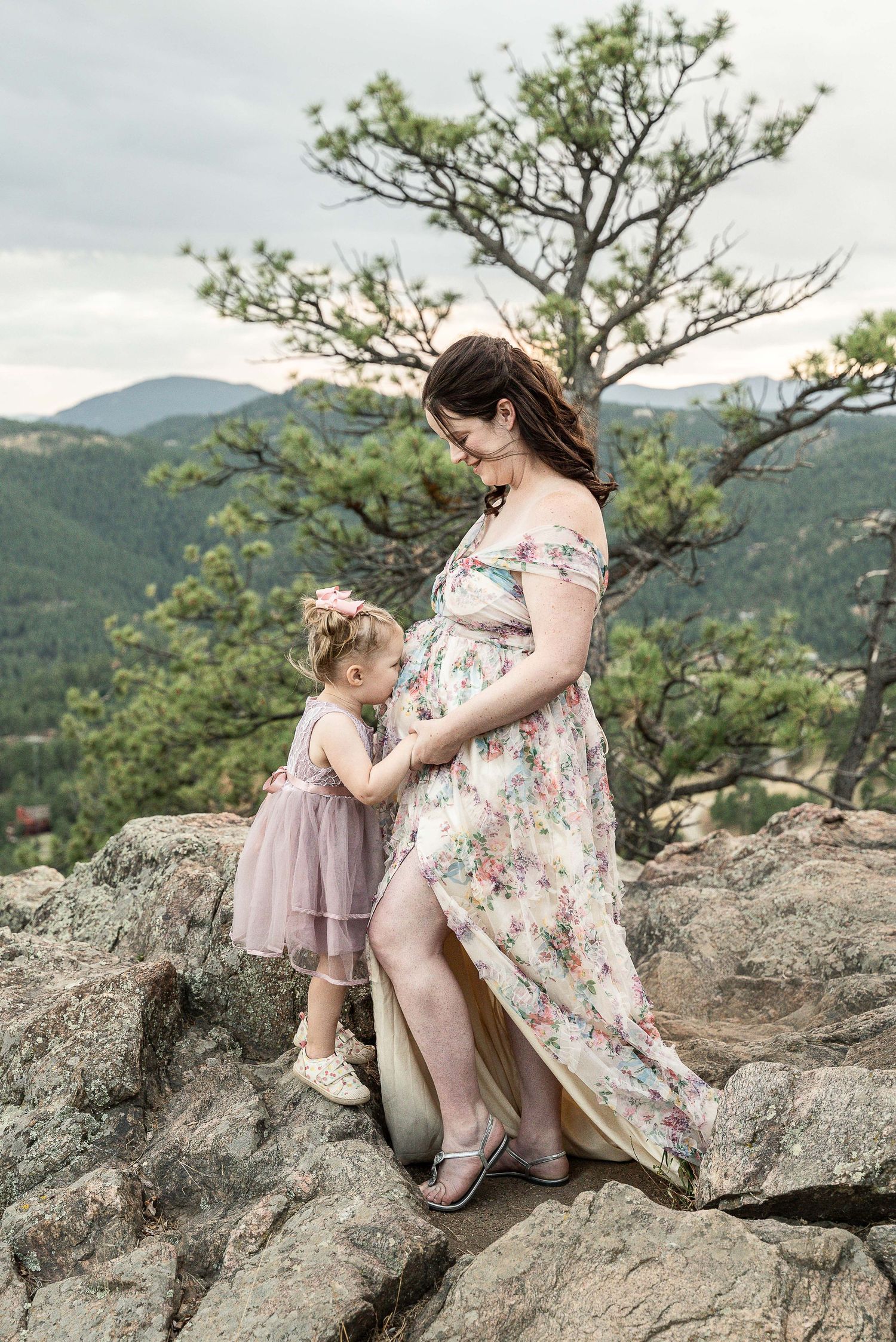 A heartfelt candid moment of family bonding on a rocky mountain overlook wearing floral and mauve dresses.