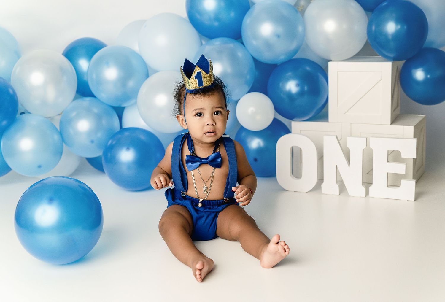 Royal blue themed first birthday setup with balloon arch and white letters.