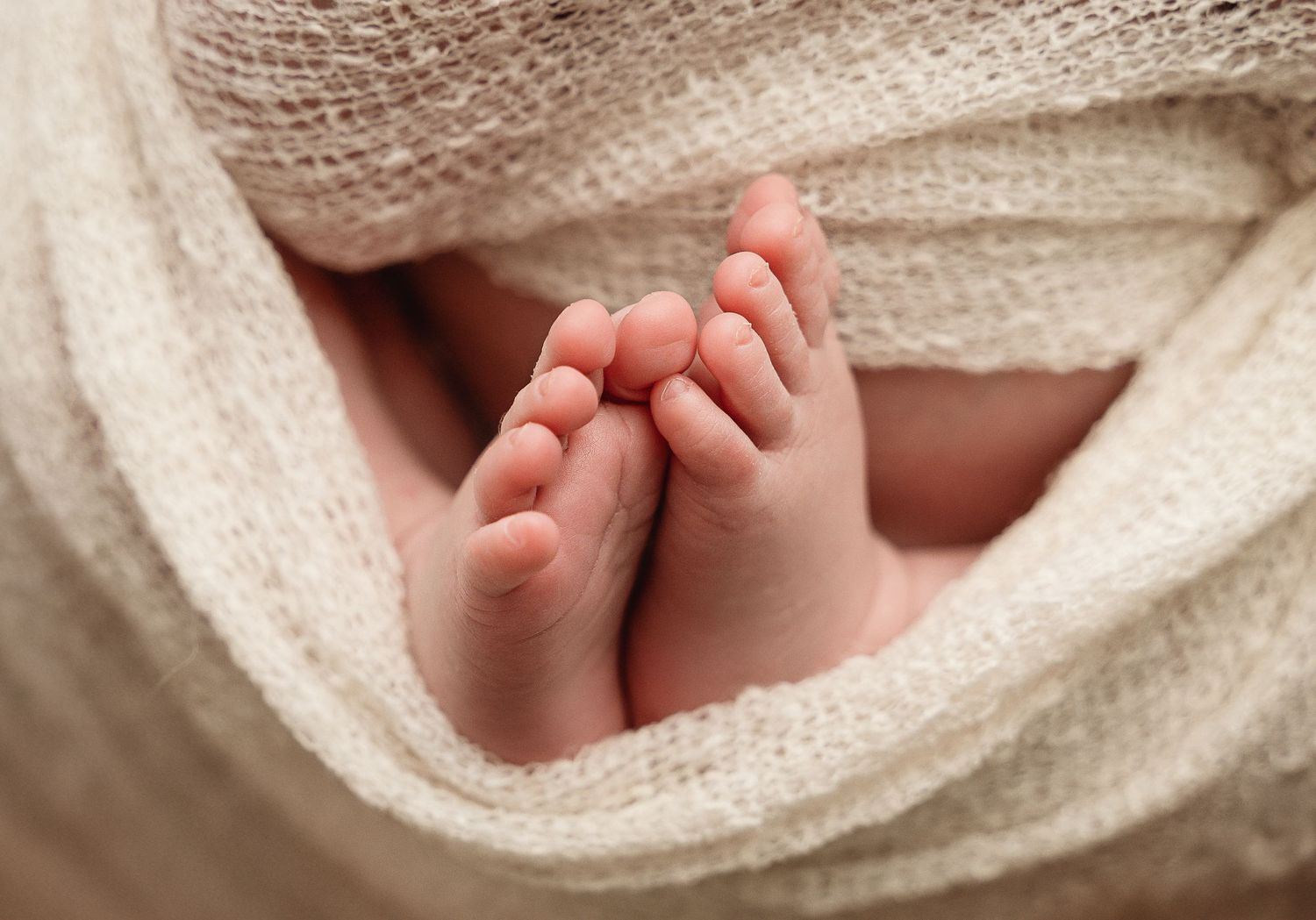 Close-up of tiny baby feet peeking through soft cream-colored blanket.